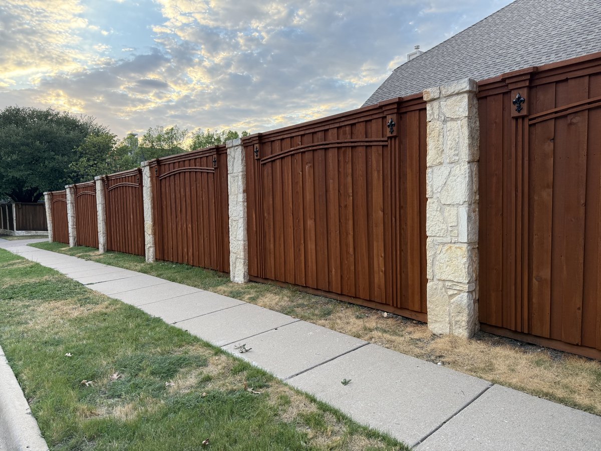 Stained wood fence with stone columns and fleur-de-lis accents