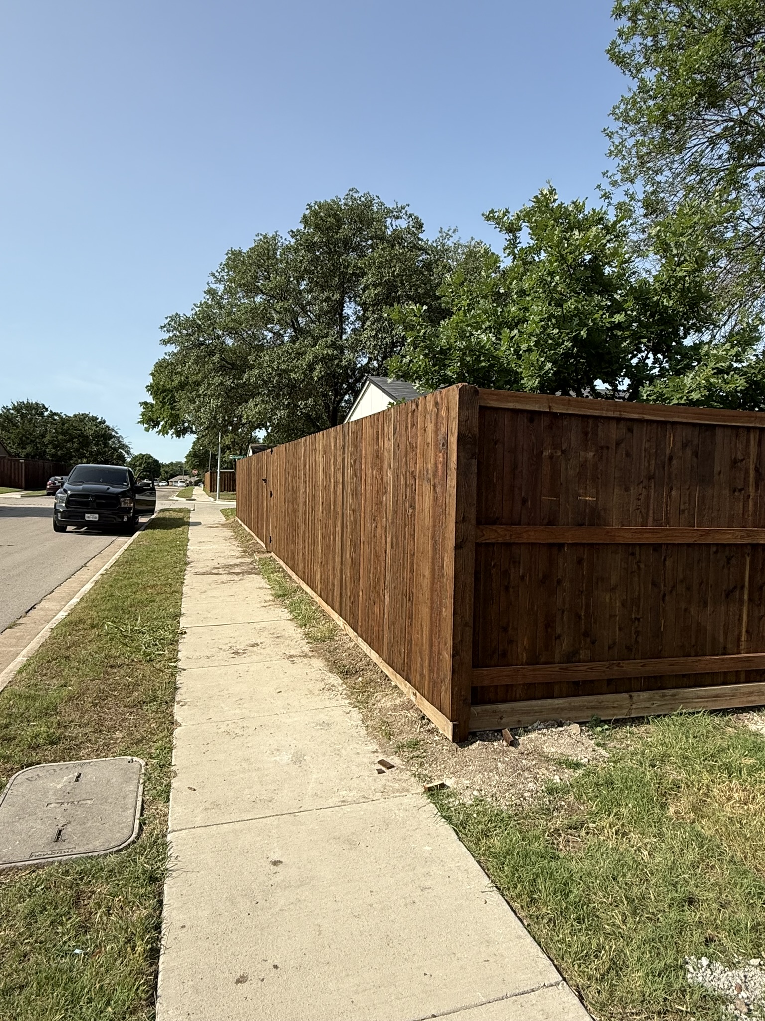 Long cedar board-on-board privacy fence running along a sidewalk with cap rail