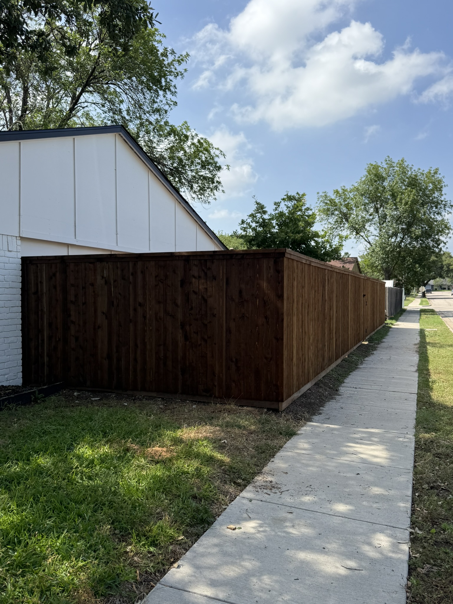 Dark-stained cedar board-on-board privacy fence alongside a white building and sidewalk