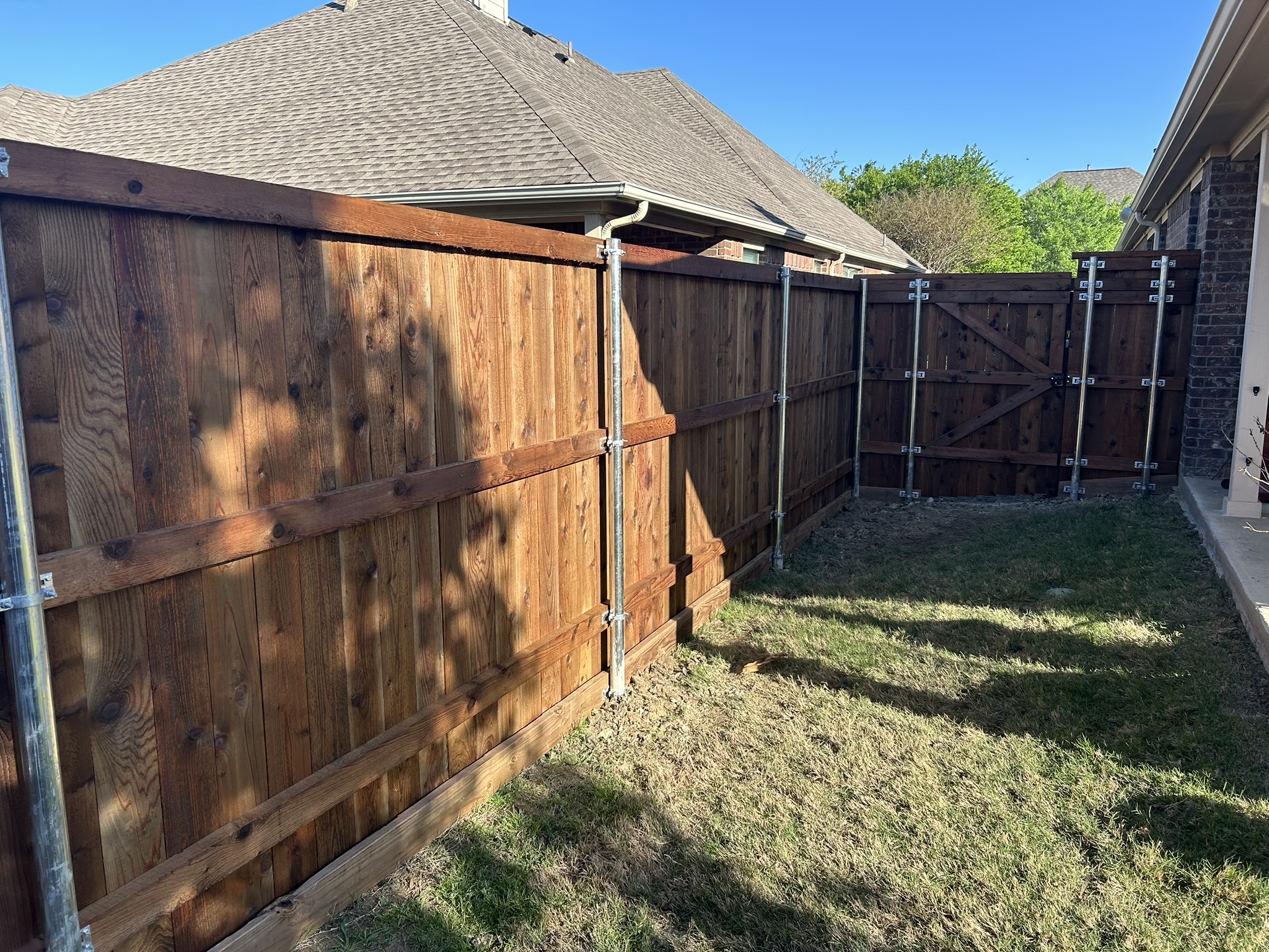 Cedar board-on-board privacy fence with metal posts and double gate viewed from back side
