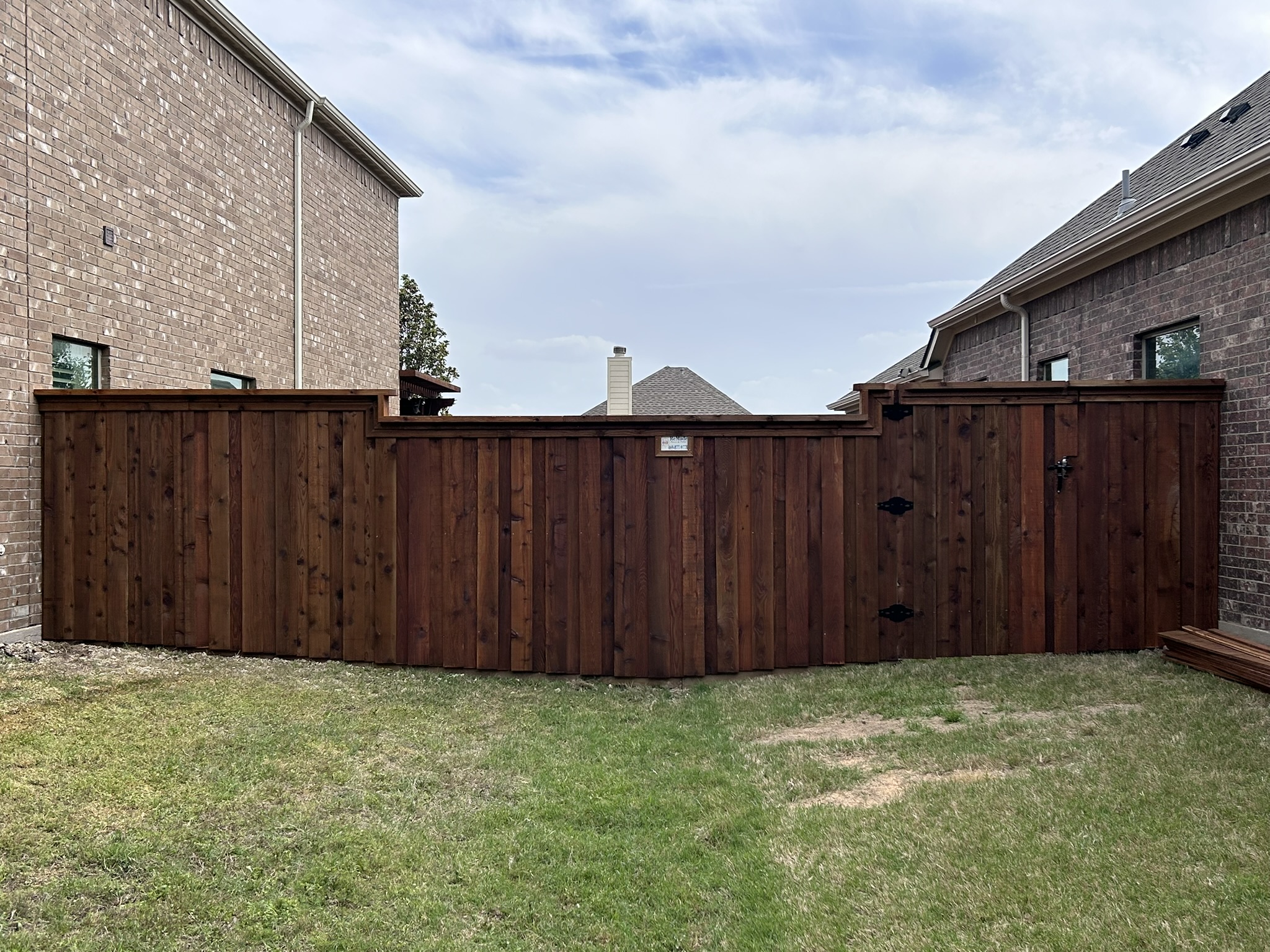 Dark-stained cedar privacy fence with stepped height and gate between brick homes