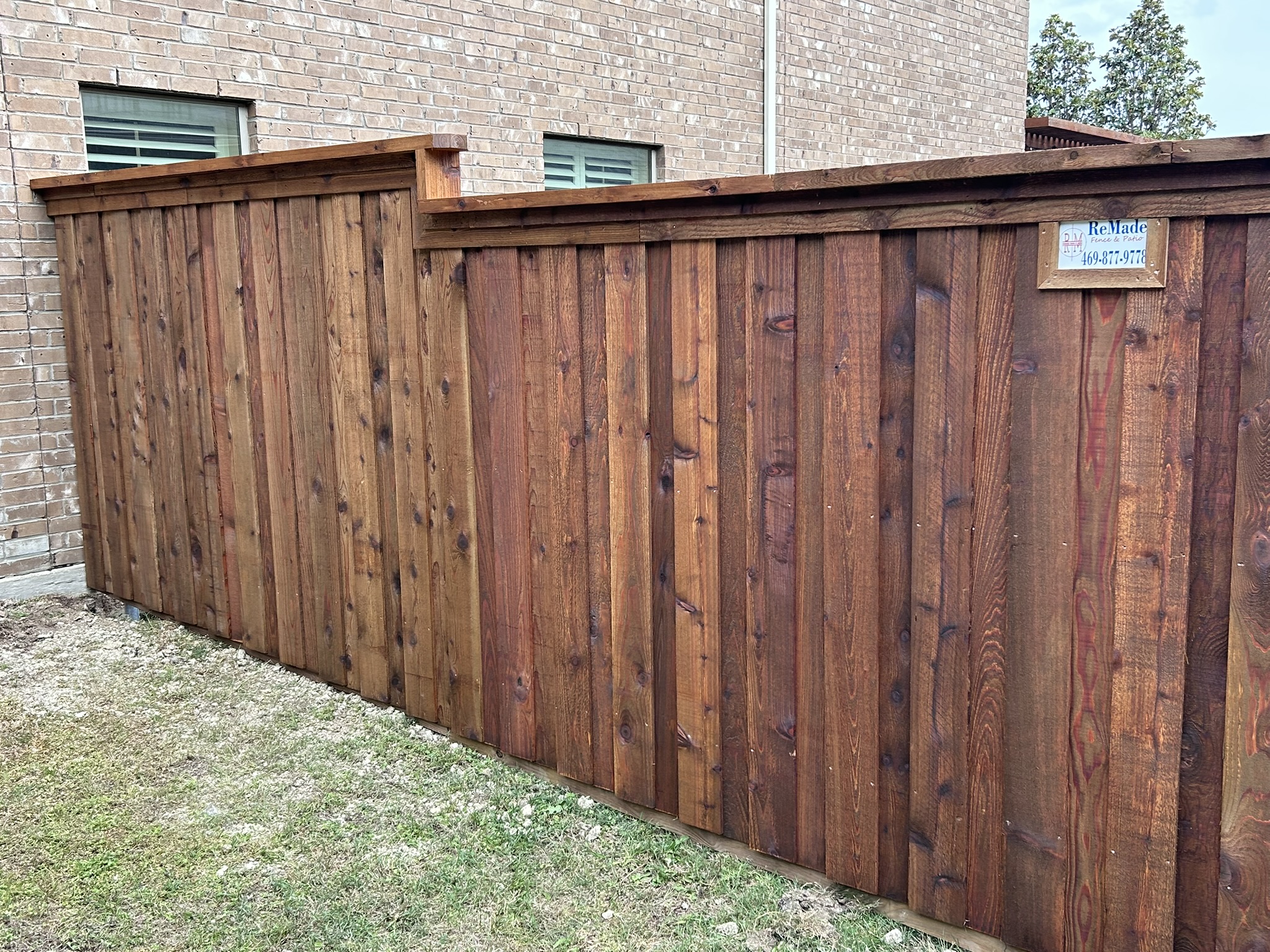 Stained cedar board-on-board privacy fence with cap rail and company sign between brick homes