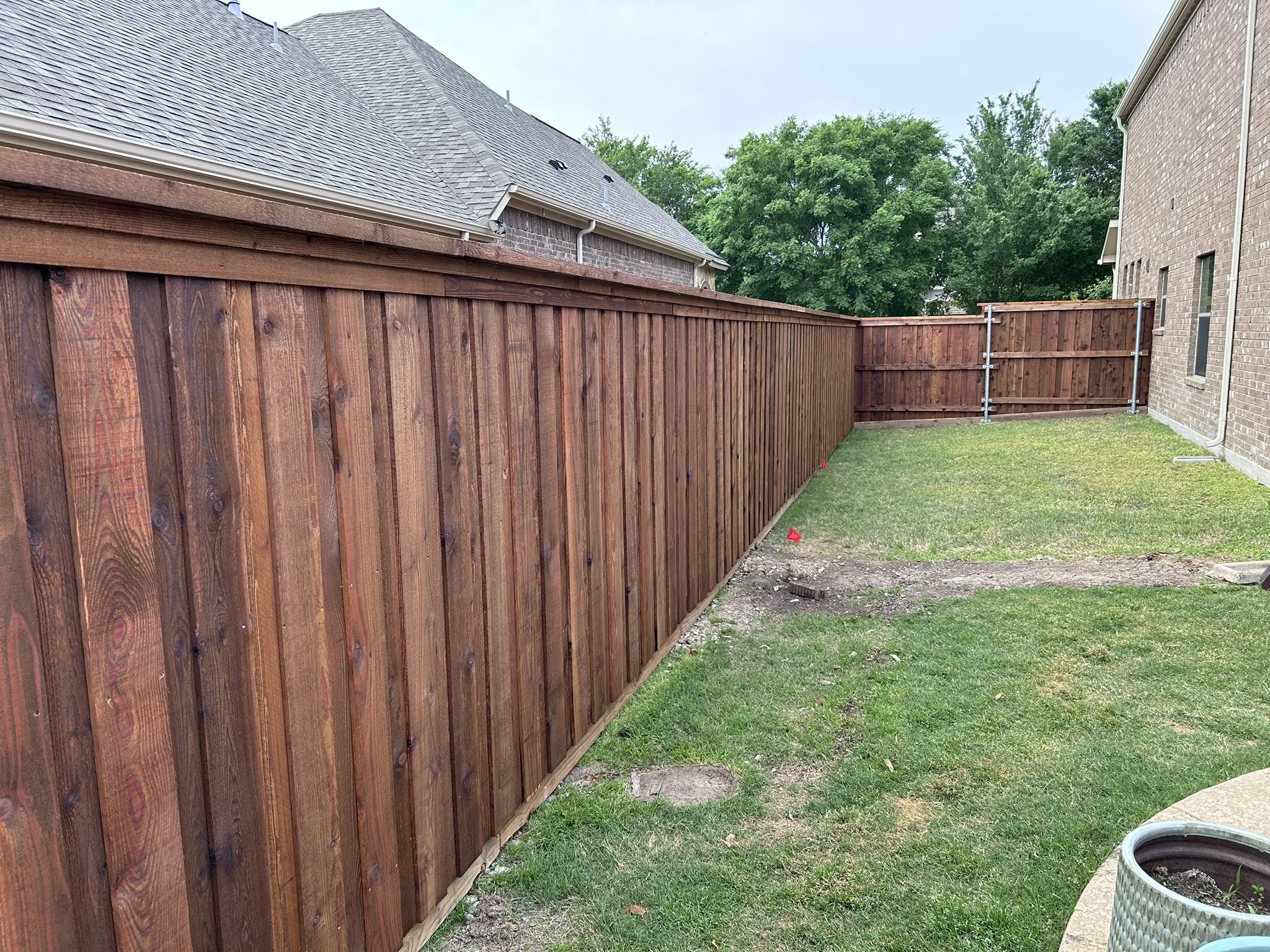 Long stained cedar board-on-board privacy fence with metal posts along a backyard