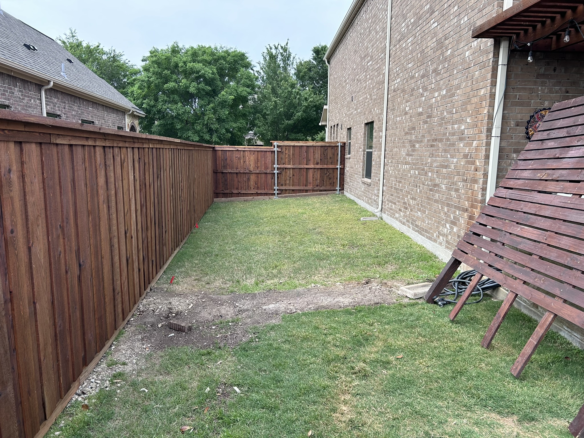 Stained cedar privacy fence along a backyard with a pergola structure visible at right