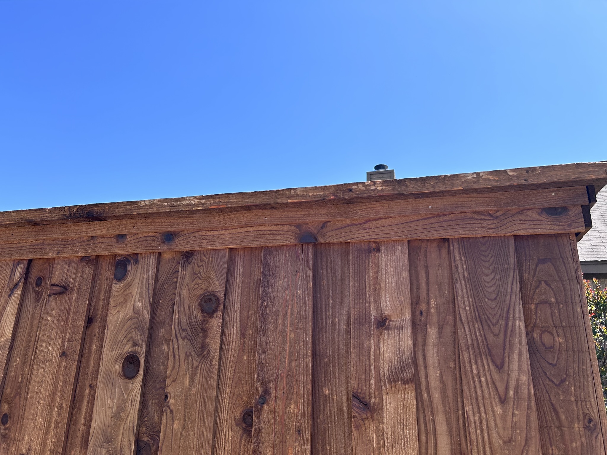 Close-up of stained cedar fence top rail and board detail against blue sky