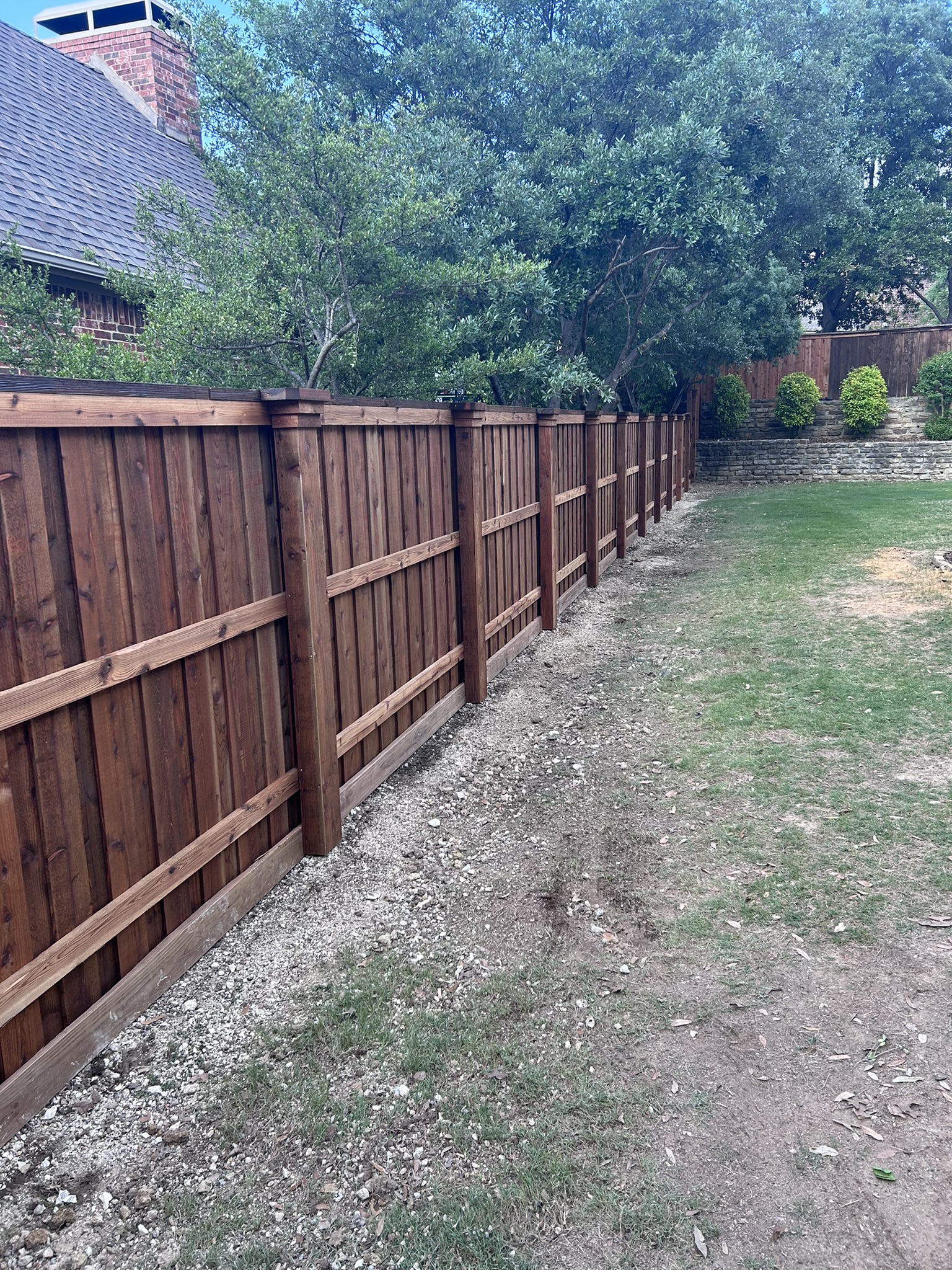 Stained cedar privacy fence with cap rail along a sloped backyard with stone retaining wall