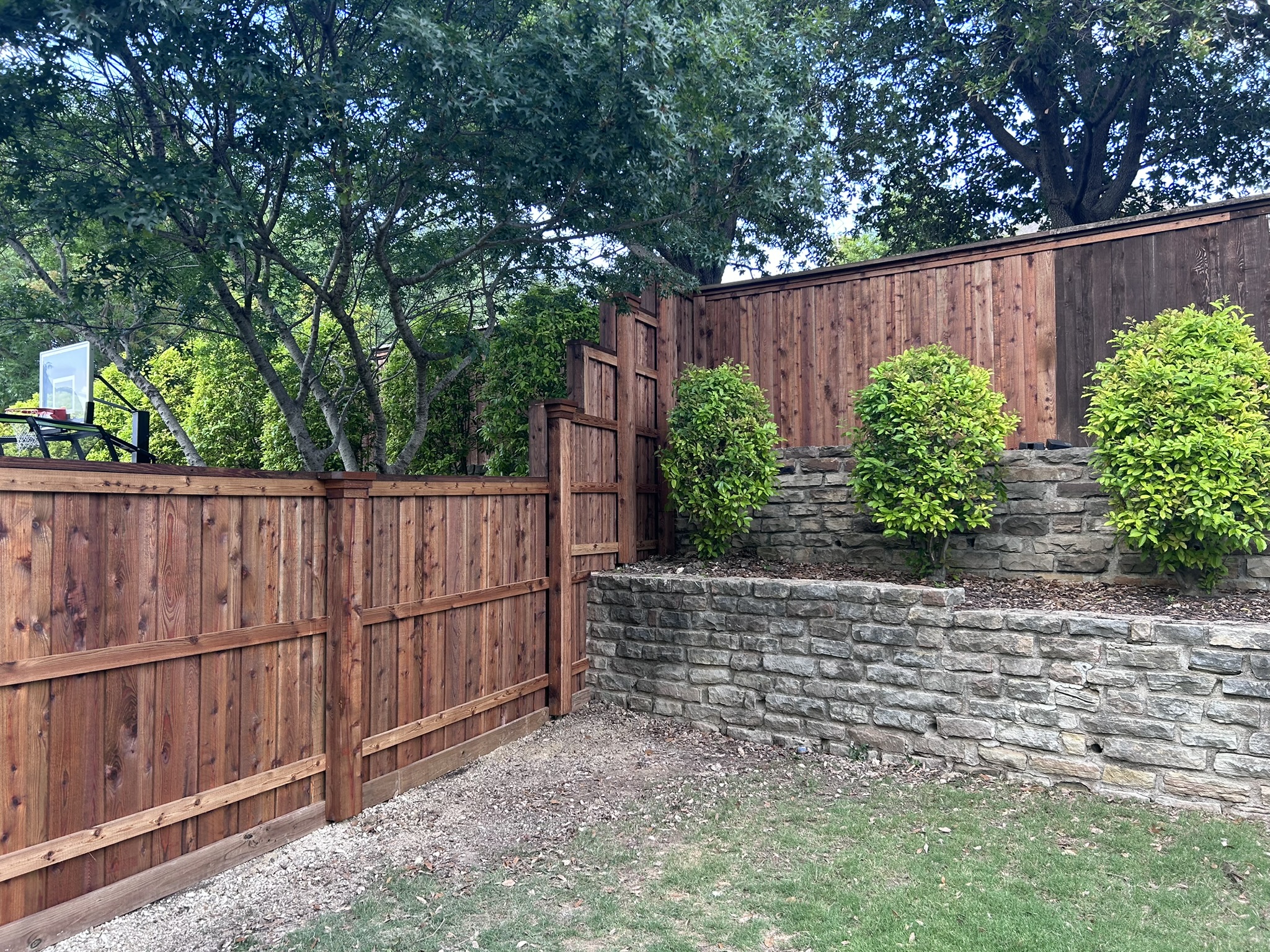 Stained cedar board-on-board privacy fence stepping down a slope with stone retaining wall