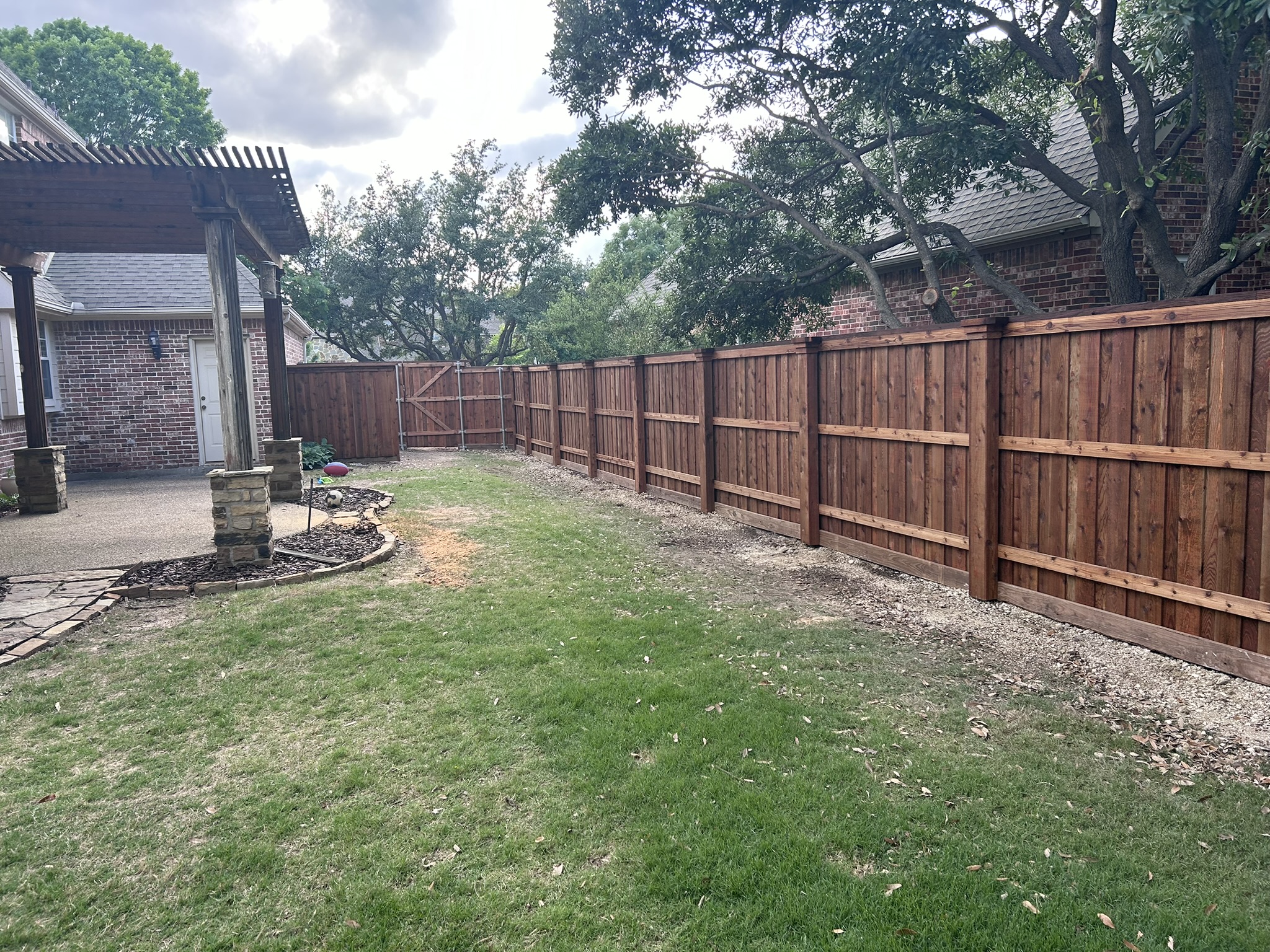 Stained cedar privacy fence in a backyard with pergola visible at left