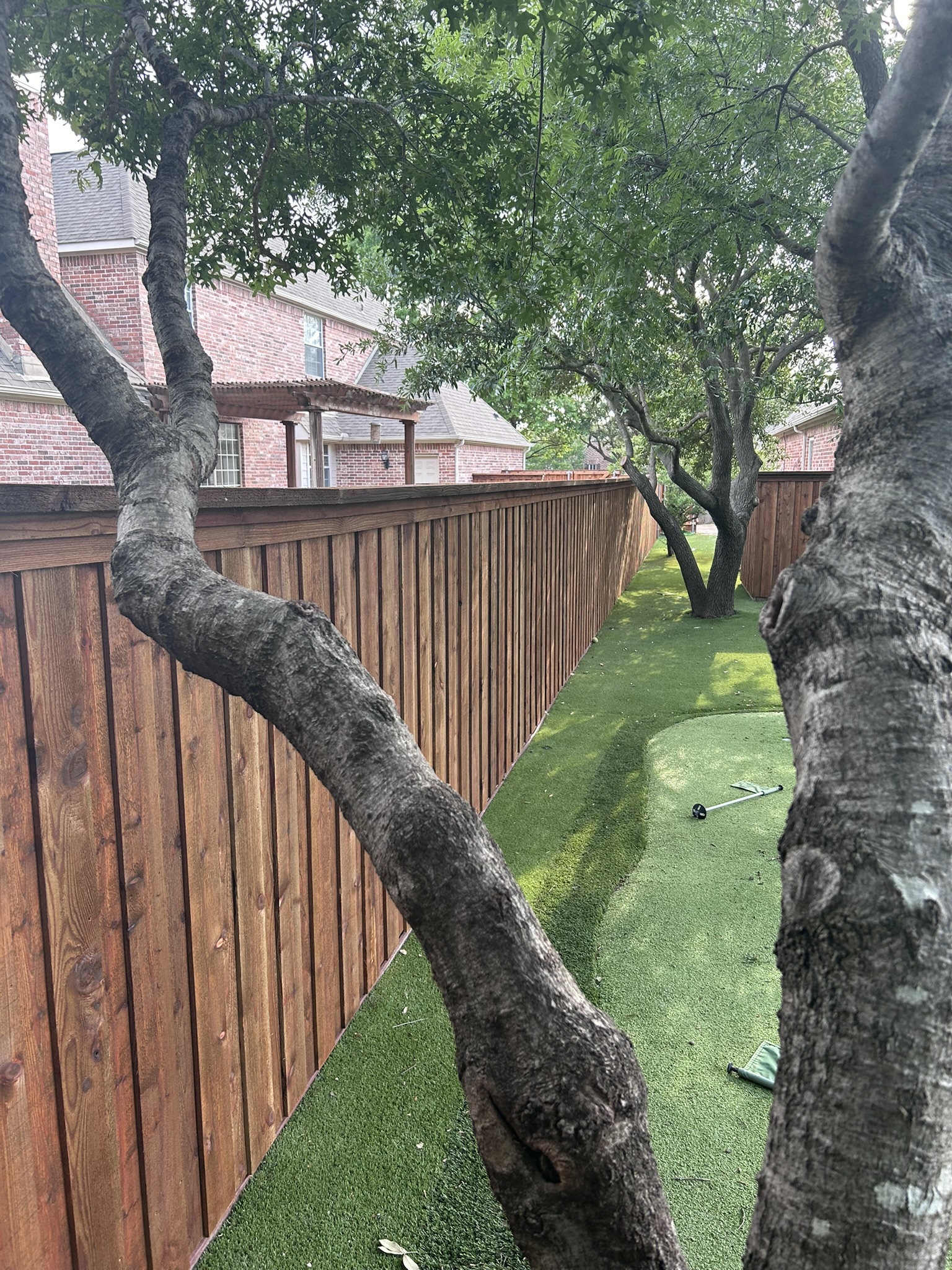 Stained cedar privacy fence viewed through mature tree branches over artificial turf