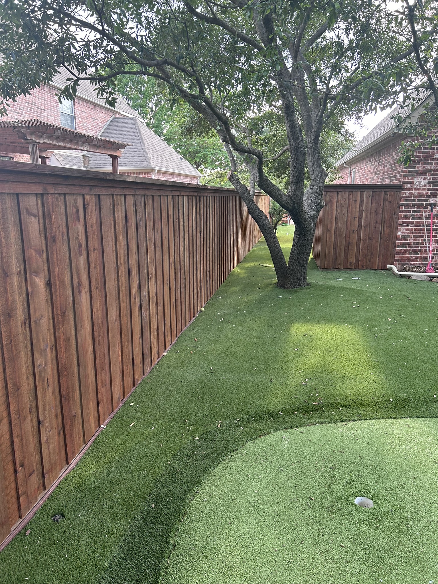 Stained cedar privacy fence along a side yard with artificial turf putting green and large tree
