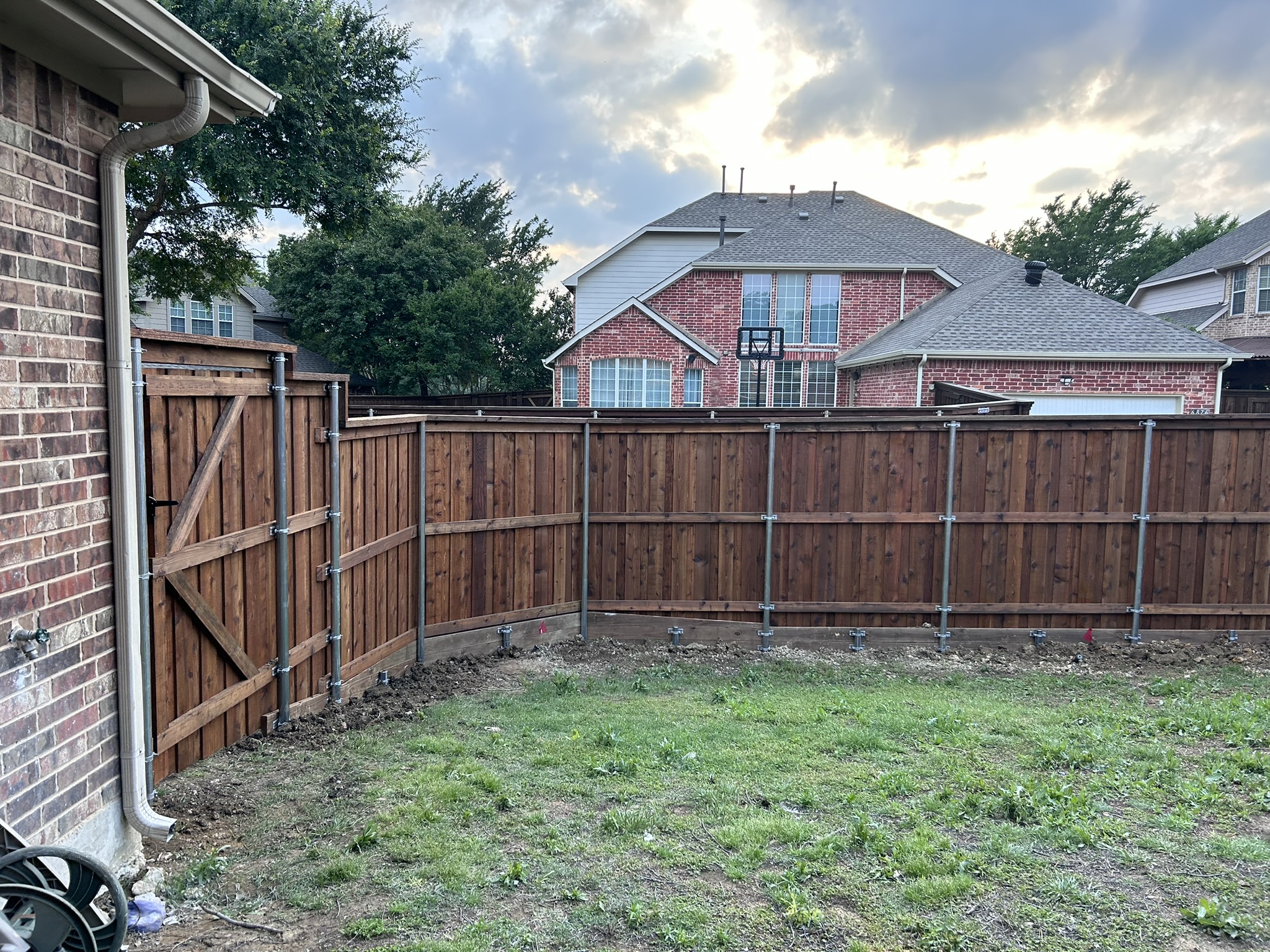 Stained cedar privacy fence with gate and metal posts in a backyard at dusk