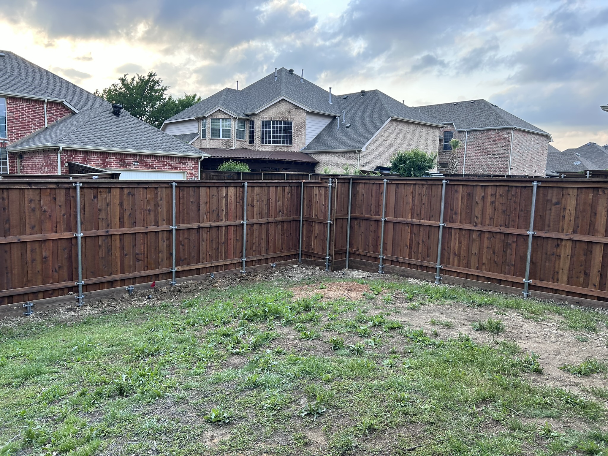 Stained cedar board-on-board privacy fence with metal posts spanning a backyard corner at dusk