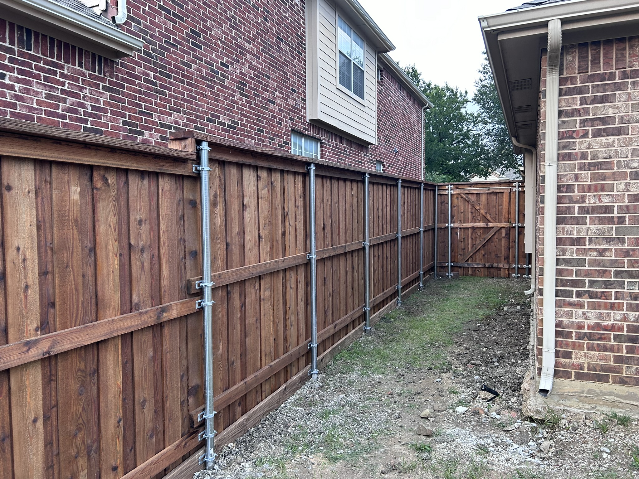 Stained cedar privacy fence with metal posts along a side yard between houses