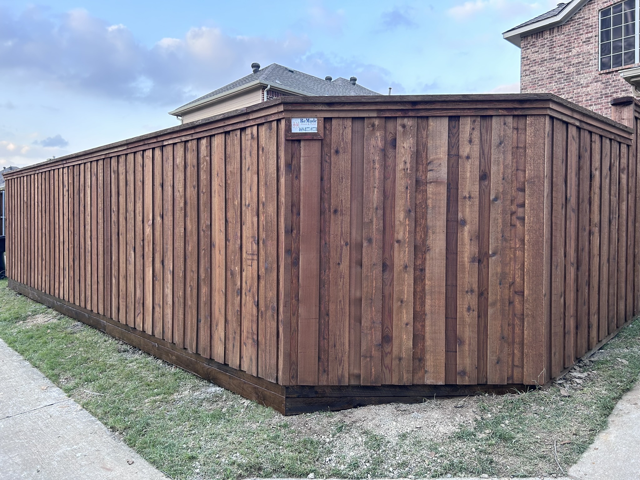 Stained cedar board-on-board privacy fence corner with company sign between brick homes