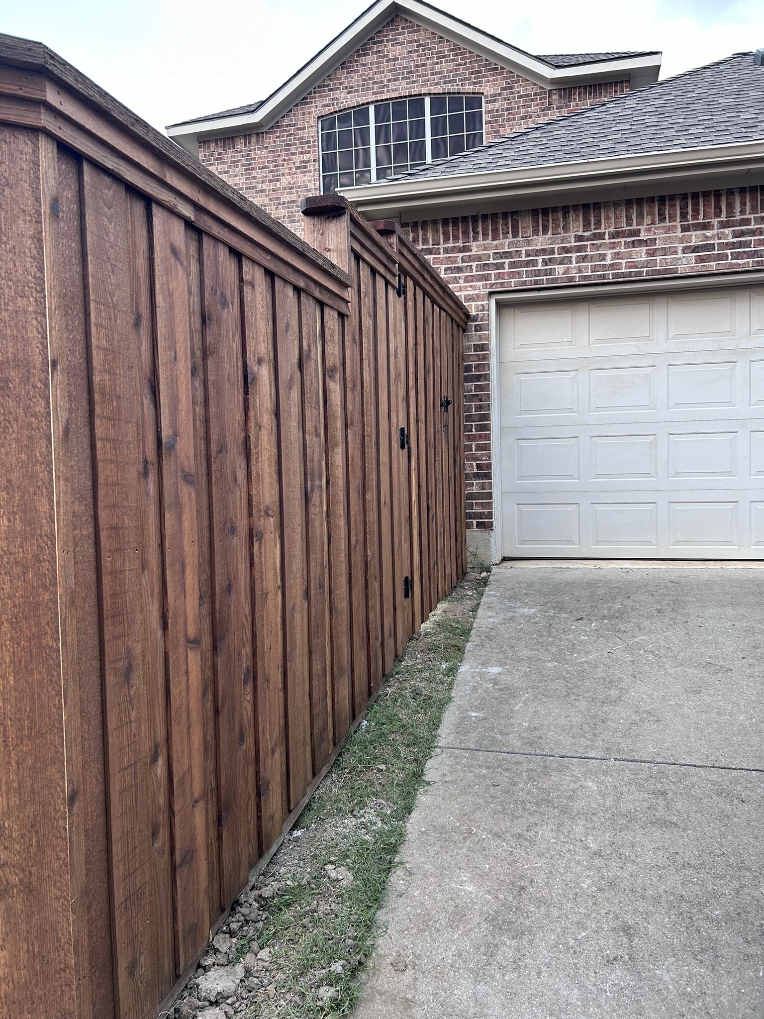 Stained cedar privacy fence with gate next to a driveway and garage