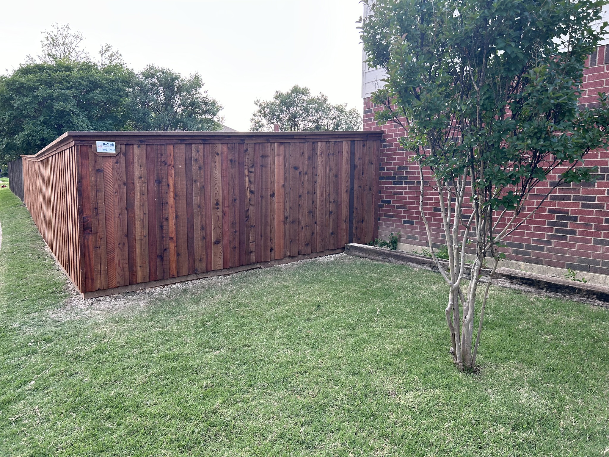 Dark-stained cedar board-on-board privacy fence corner with cap rail next to a brick house