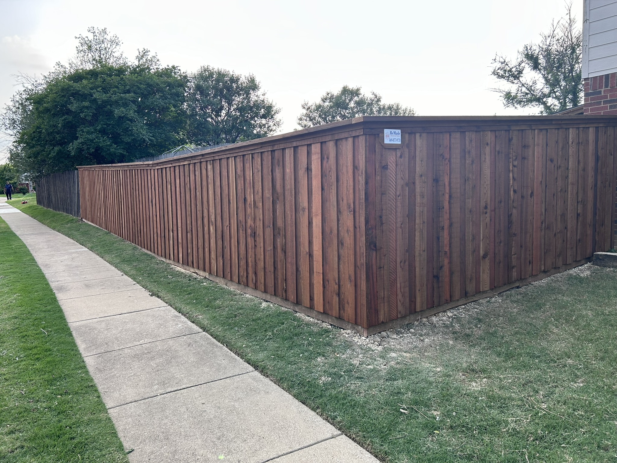 Long dark-stained cedar board-on-board privacy fence with cap rail along a sidewalk