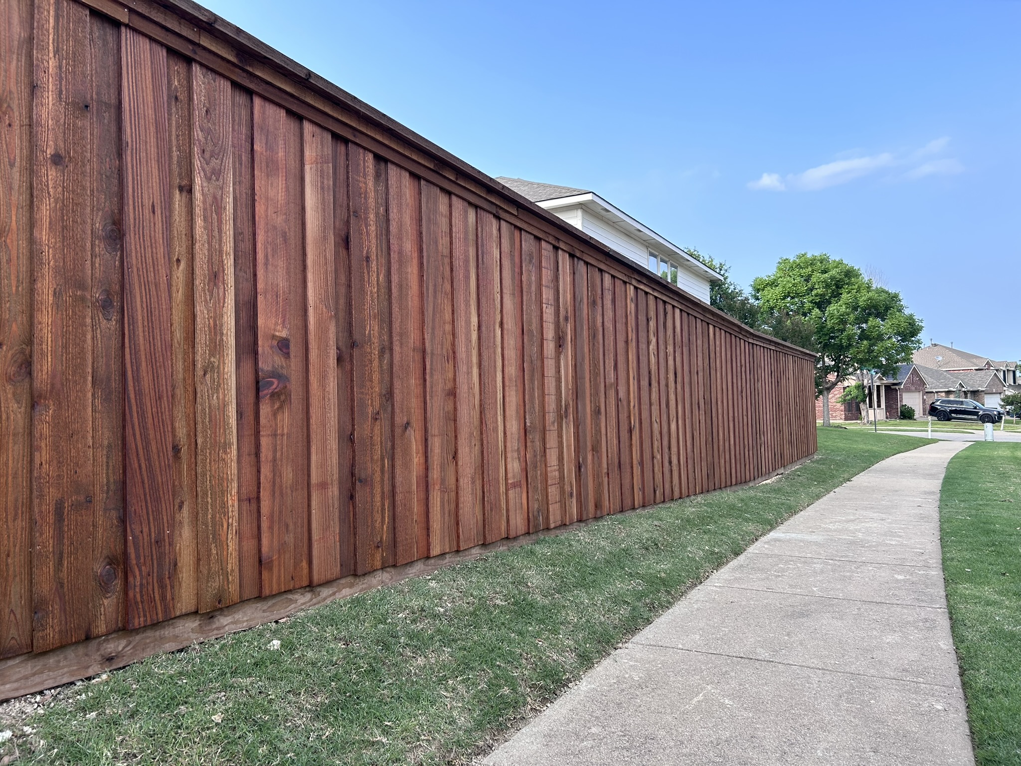 Stained cedar board-on-board privacy fence extending along a sidewalk with houses in background