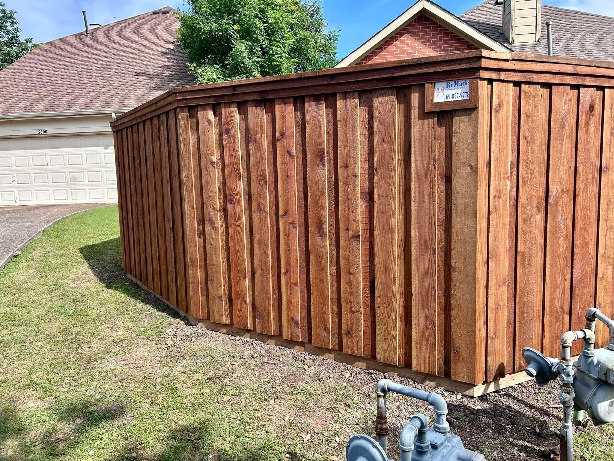 Stained cedar board-on-board privacy fence corner section near a garage and yard