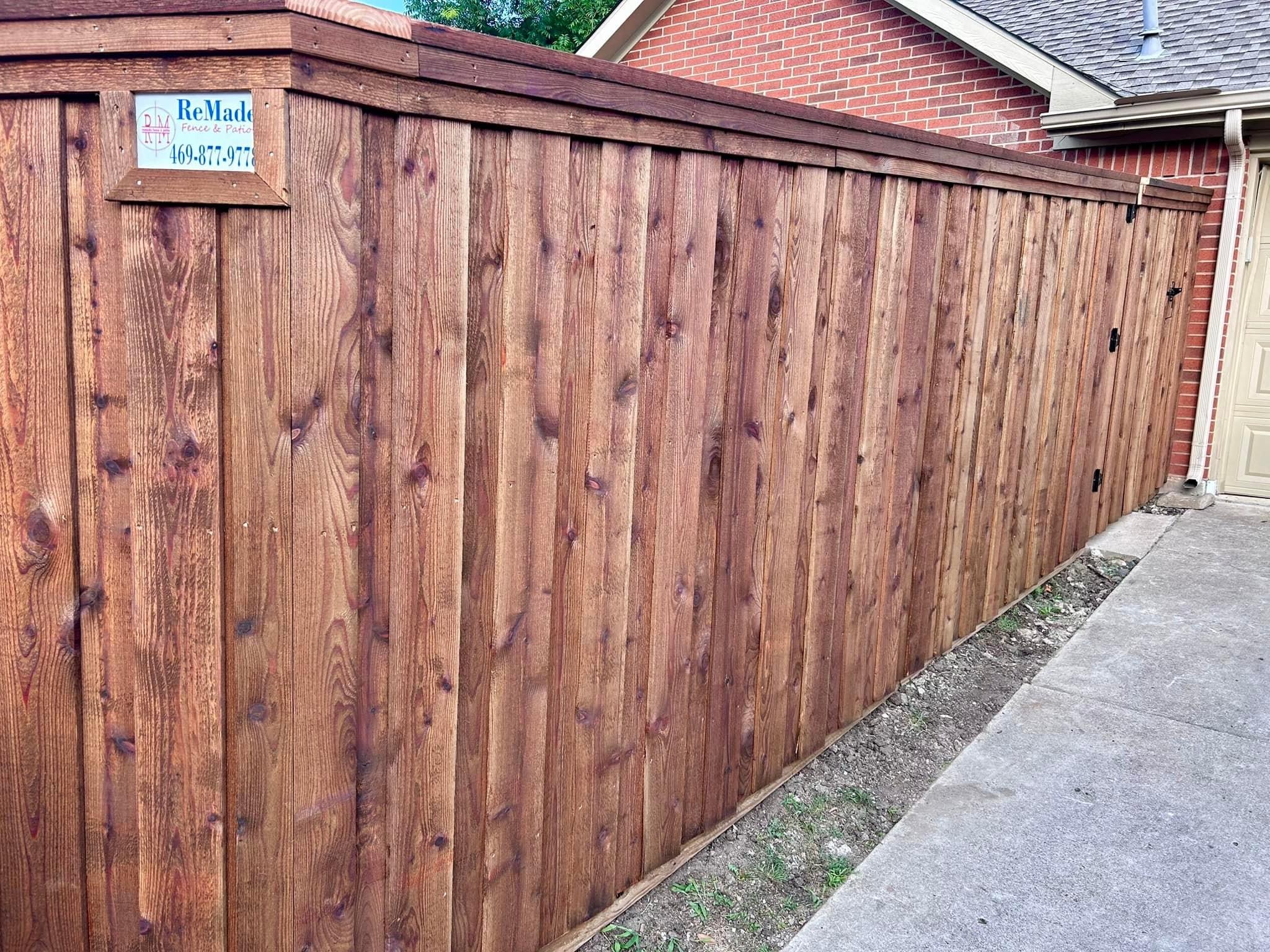 Stained cedar board-on-board privacy fence with ReMade Fence company sign between houses