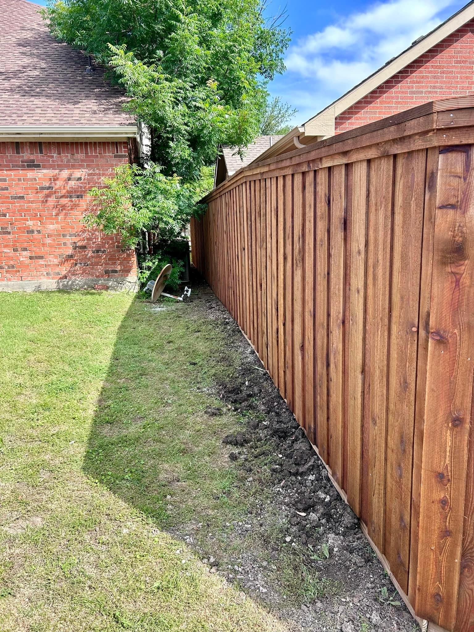 Stained cedar board-on-board privacy fence running along a side yard between brick homes