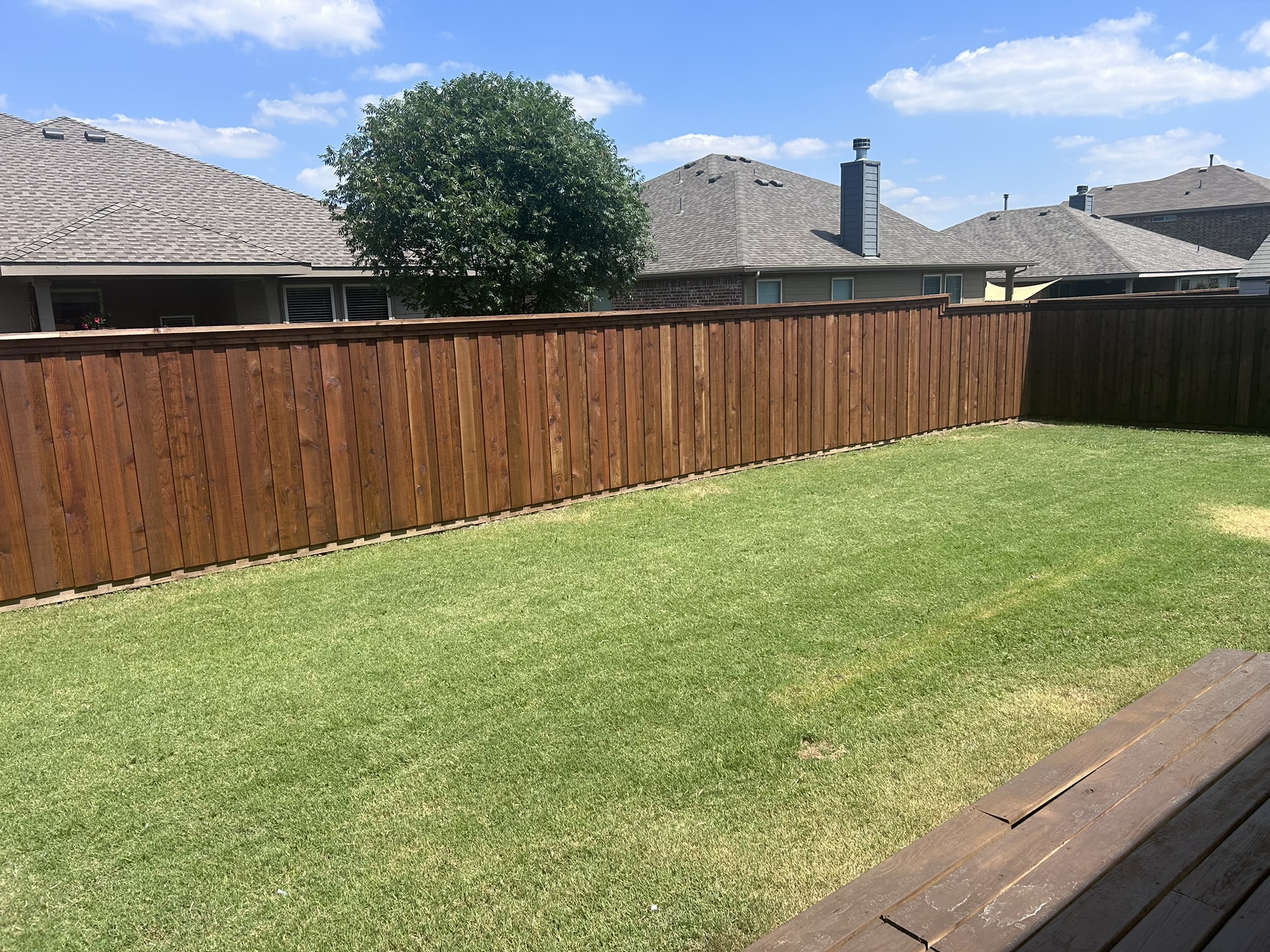 Long stained cedar board-on-board privacy fence bordering a green backyard lawn
