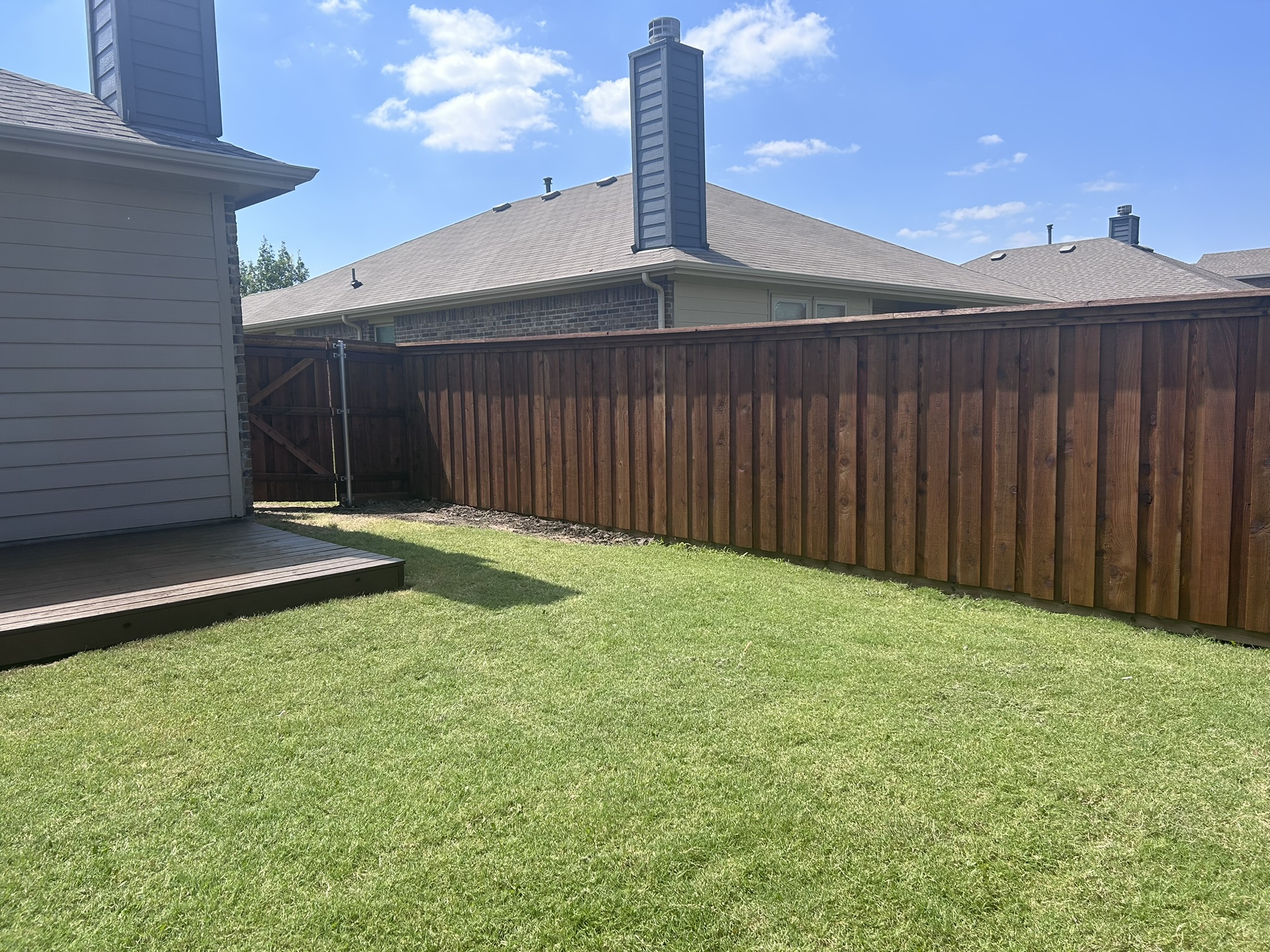 Stained cedar privacy fence in a backyard with a wood deck platform visible