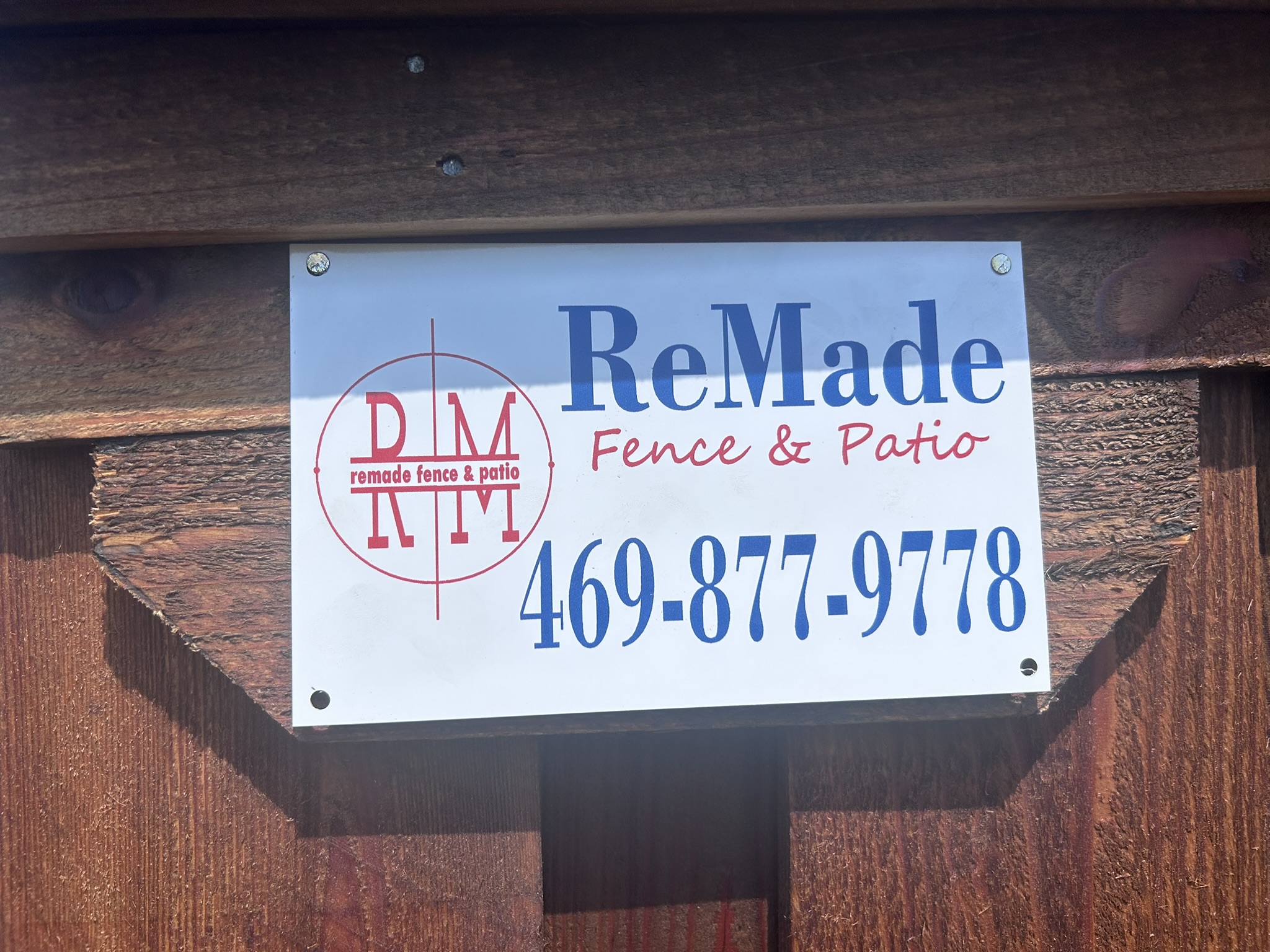 Close-up of ReMade Fence and Patio company sign mounted on a stained cedar fence