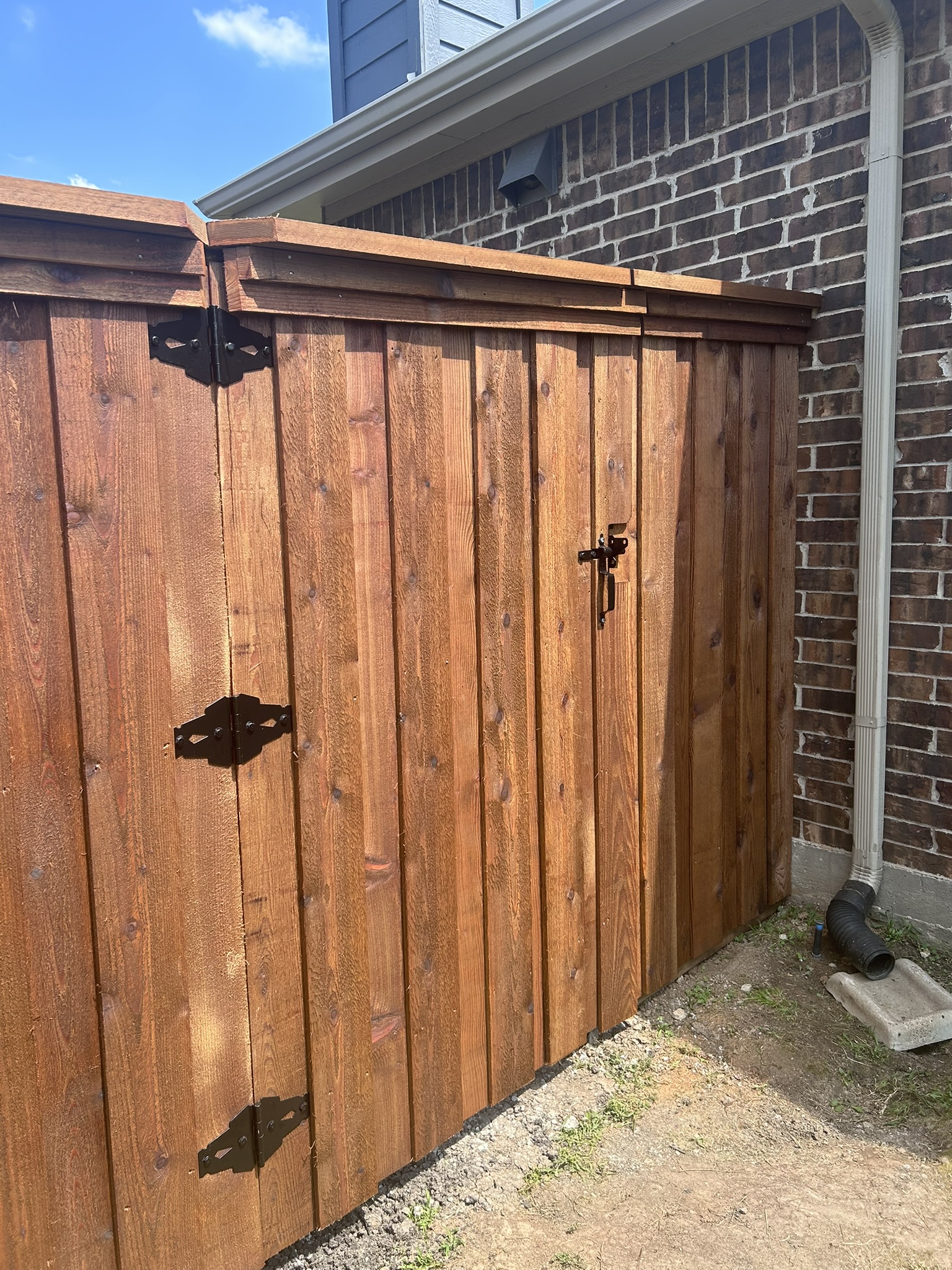 Stained cedar privacy fence with gate and decorative iron hardware along brick house