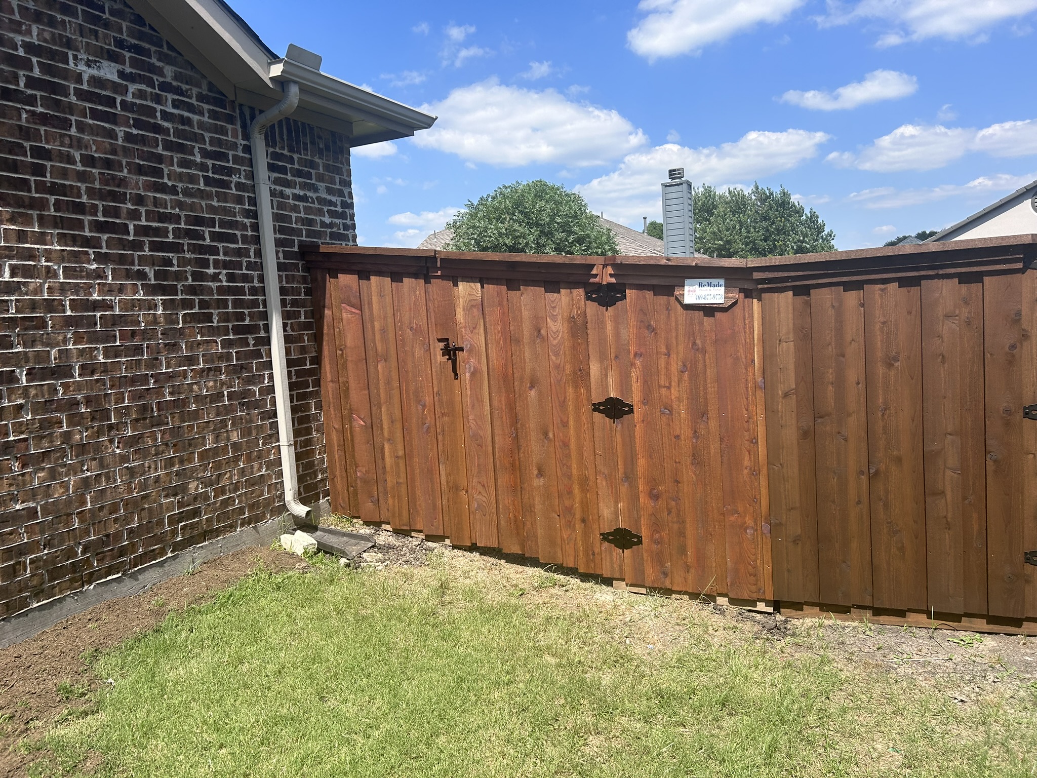 Stained cedar privacy fence and gate with decorative iron hinges between brick homes