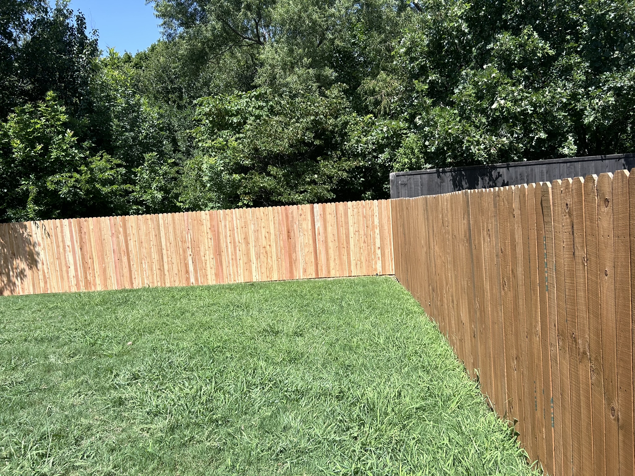 Unstained cedar stockade privacy fence corner section in a green backyard