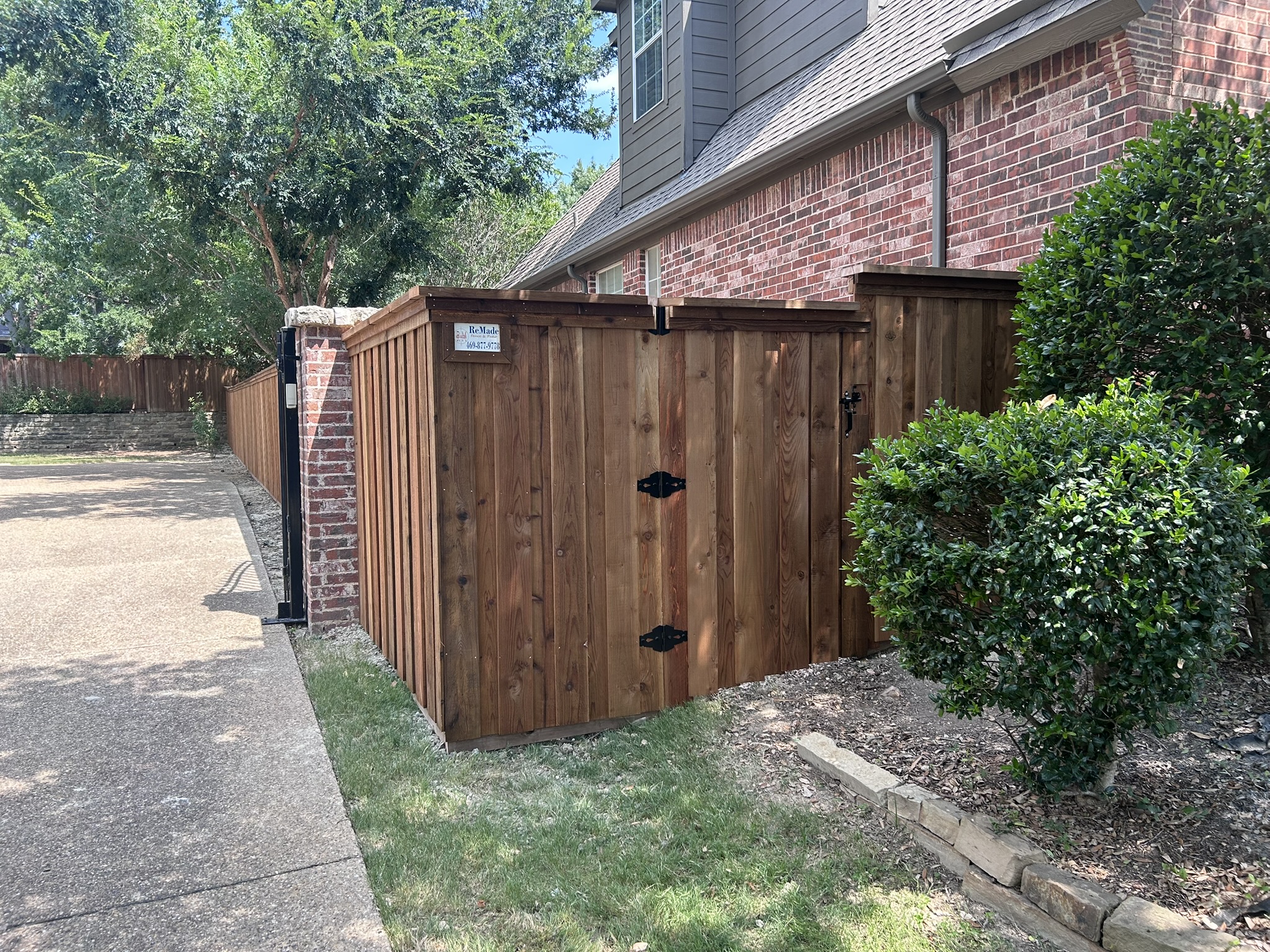 Stained cedar board-on-board privacy fence with gate and decorative hardware along a driveway