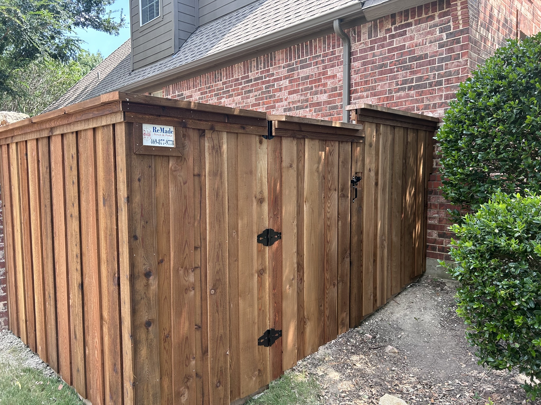 Stained cedar privacy fence and gate close-up with company sign near brick house