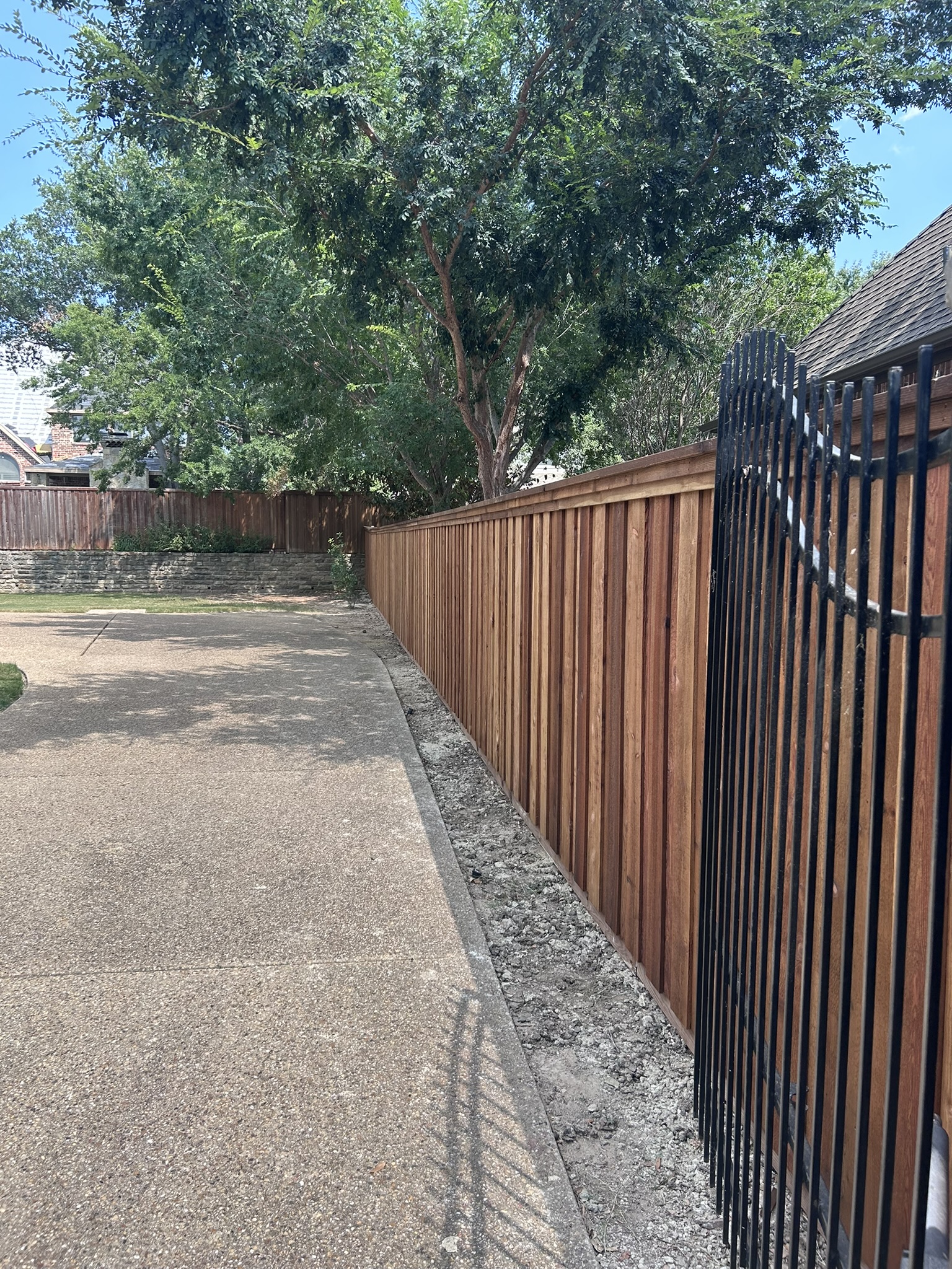 Stained cedar privacy fence with metal iron gate visible at the end along a driveway
