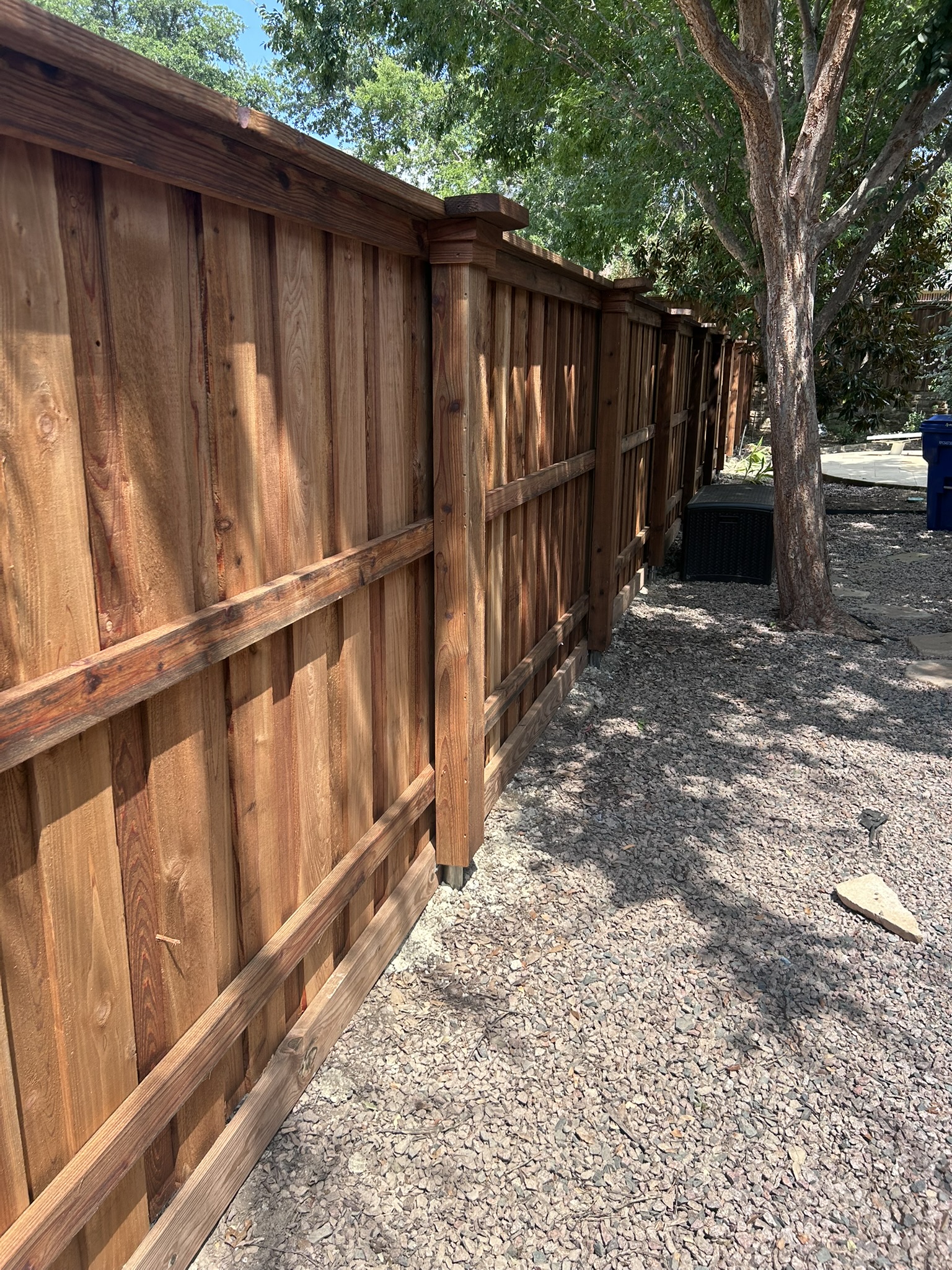 Back side of stained cedar fence showing horizontal rails and posts with tree shade