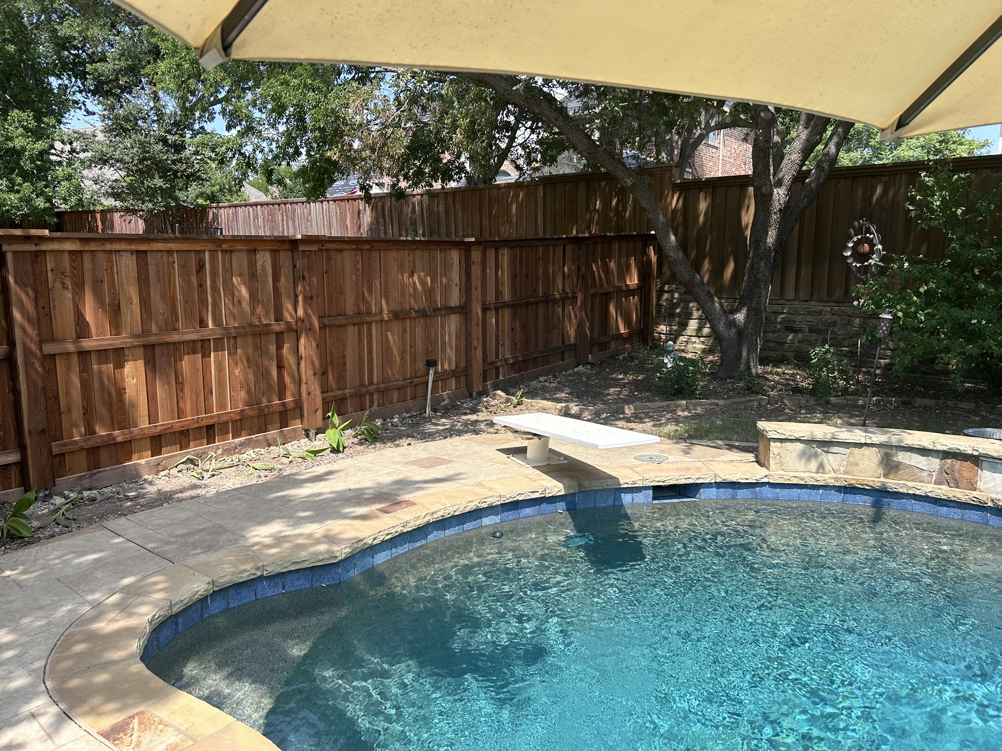 Stained cedar privacy fence surrounding a backyard pool area with shade sail overhead
