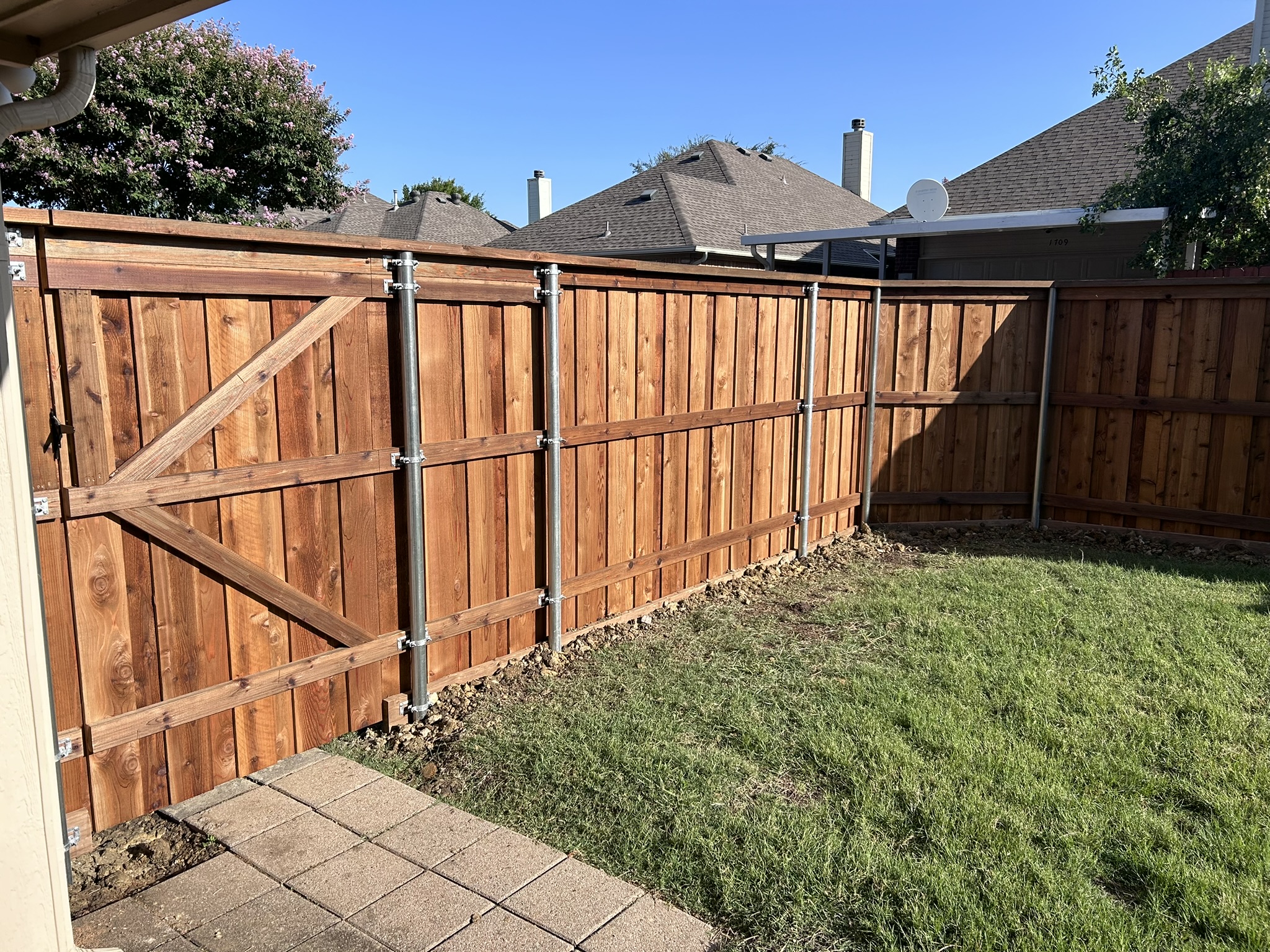 Stained cedar board-on-board fence with metal posts showing back brace structure