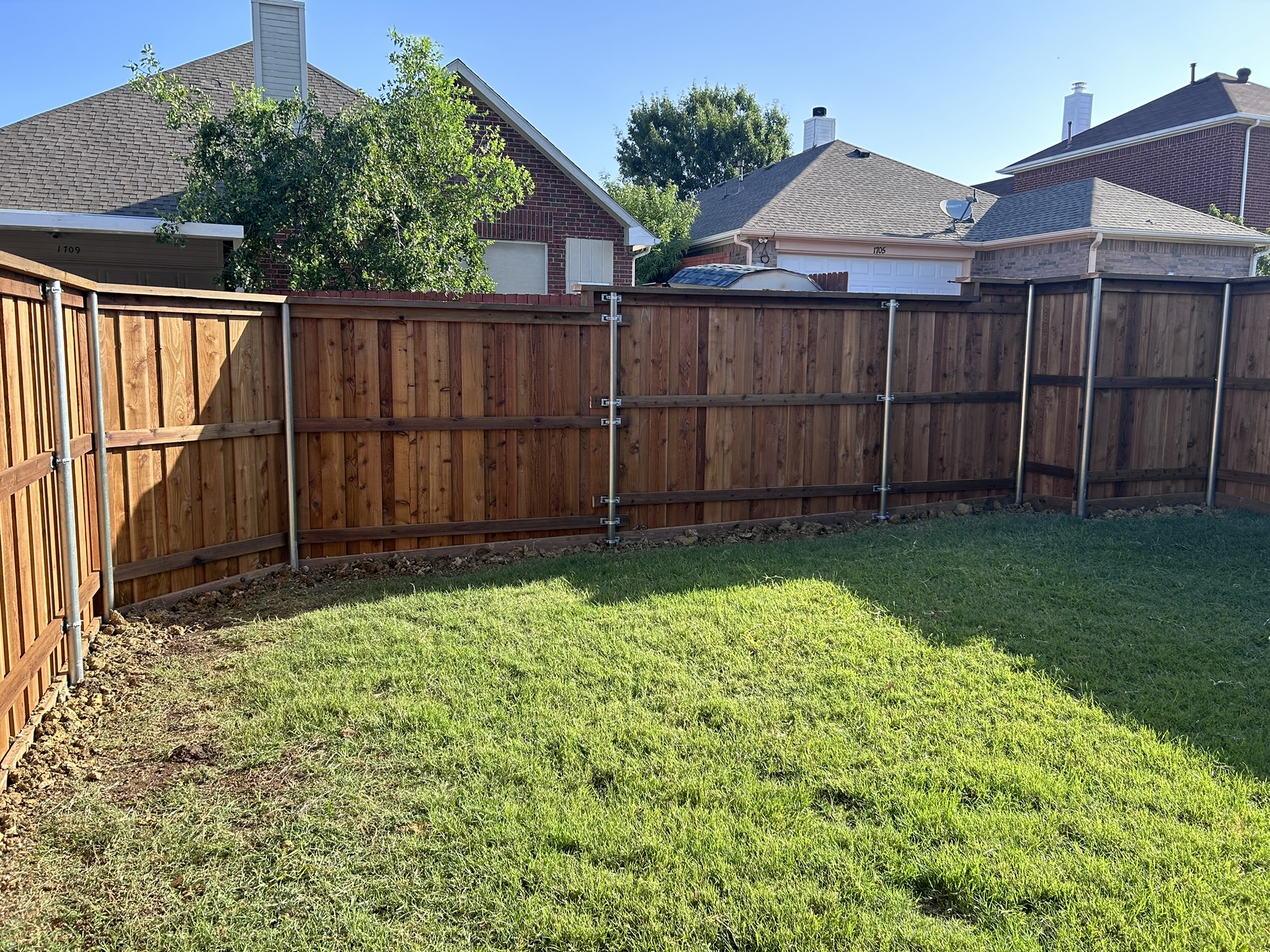 Stained cedar privacy fence with metal posts from backyard view showing multiple panels