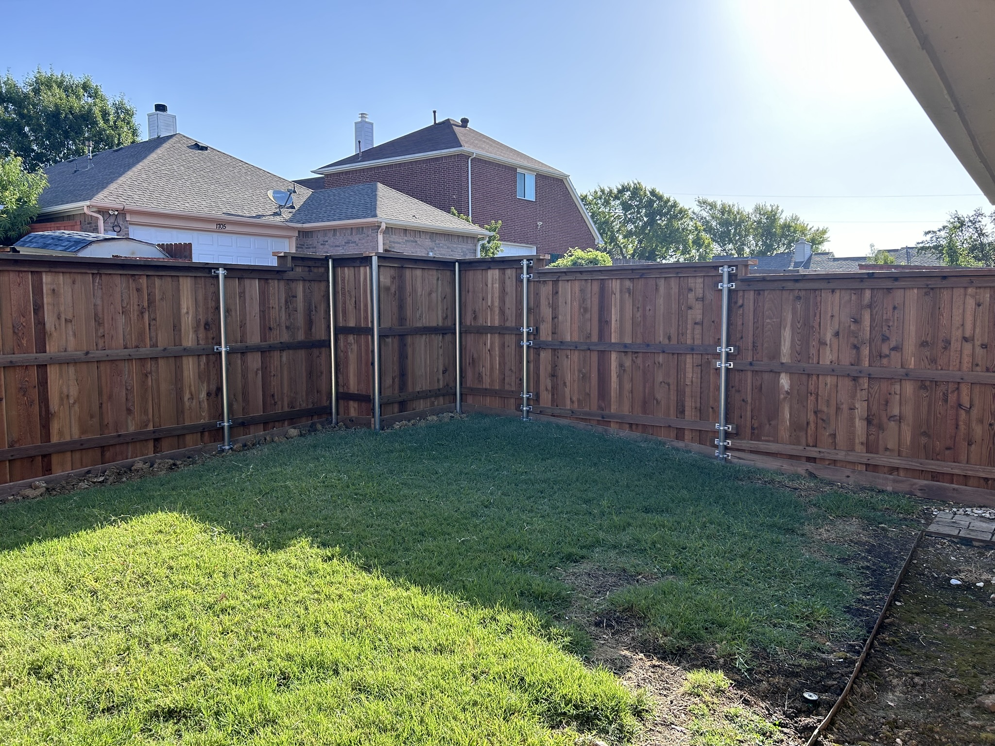 Wide view of stained cedar privacy fence with metal posts enclosing a backyard
