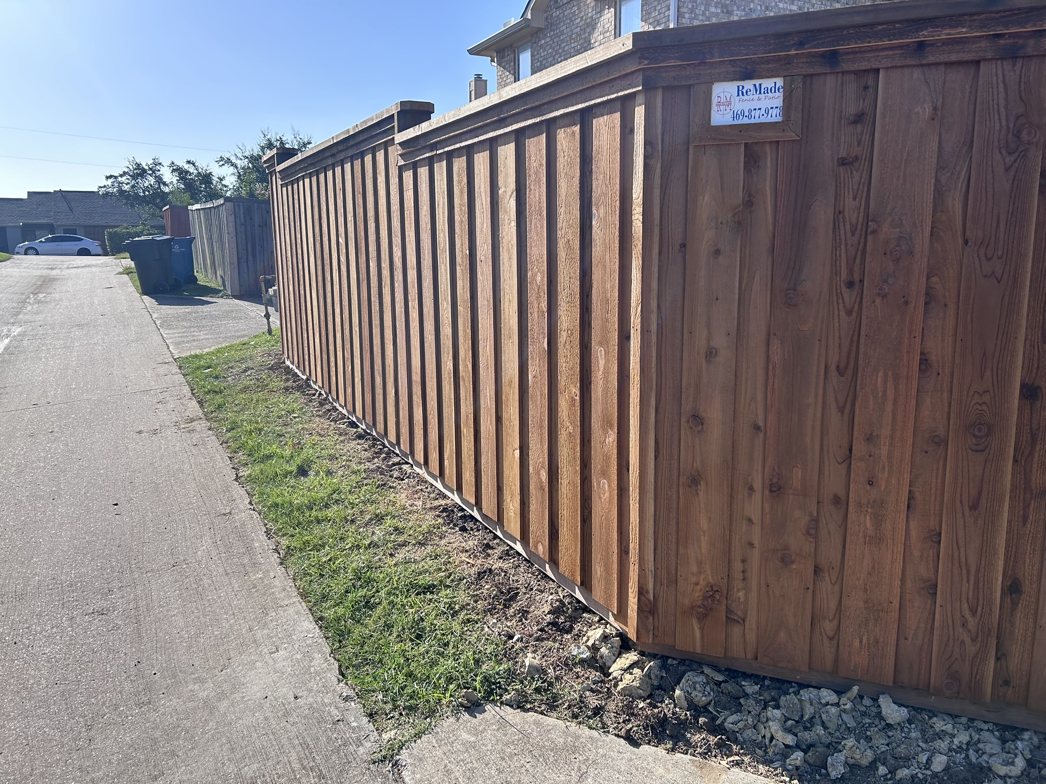 Stained cedar board-on-board privacy fence along an alley with company sign visible