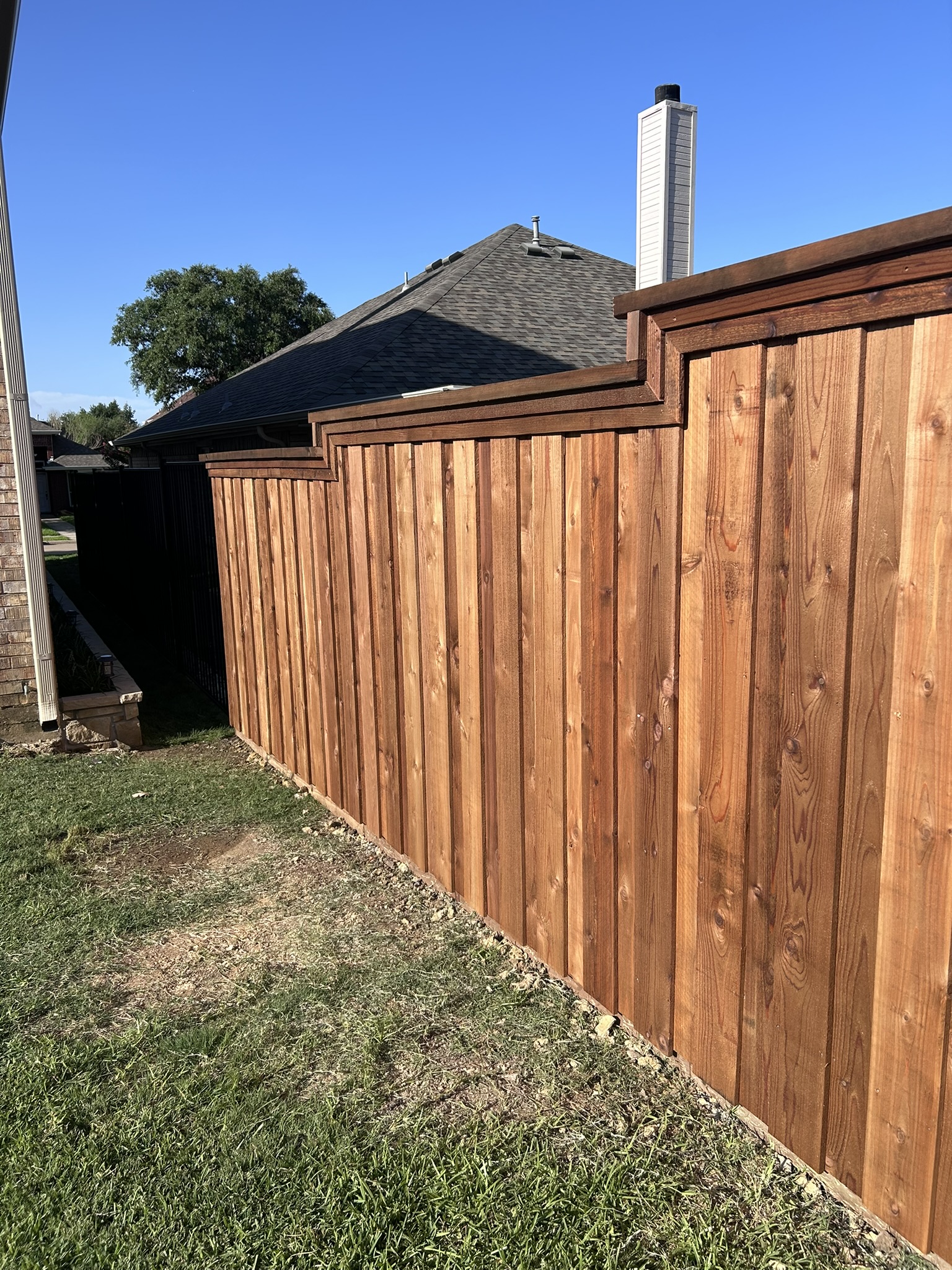 Stained cedar privacy fence with cap rail stepping down a slope beside a house