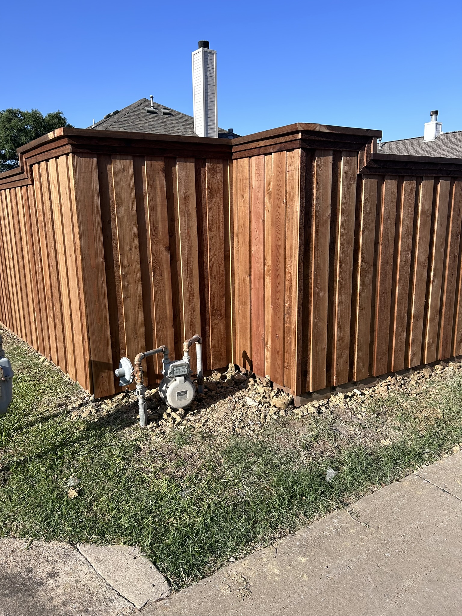 Stained cedar privacy fence corner with cap rail near a gas meter and utilities