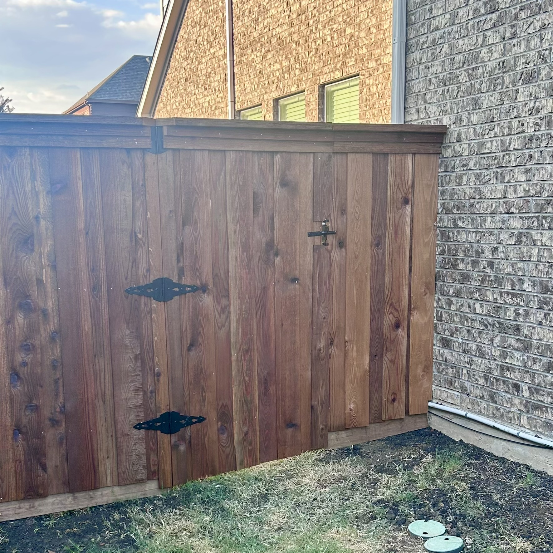 Dark stained cedar privacy fence gate with decorative iron hinges next to brick house