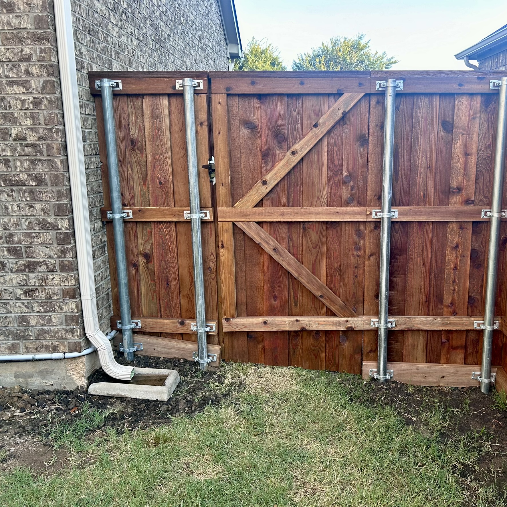Cedar wood double gate with metal posts and cross-brace framing beside a brick house