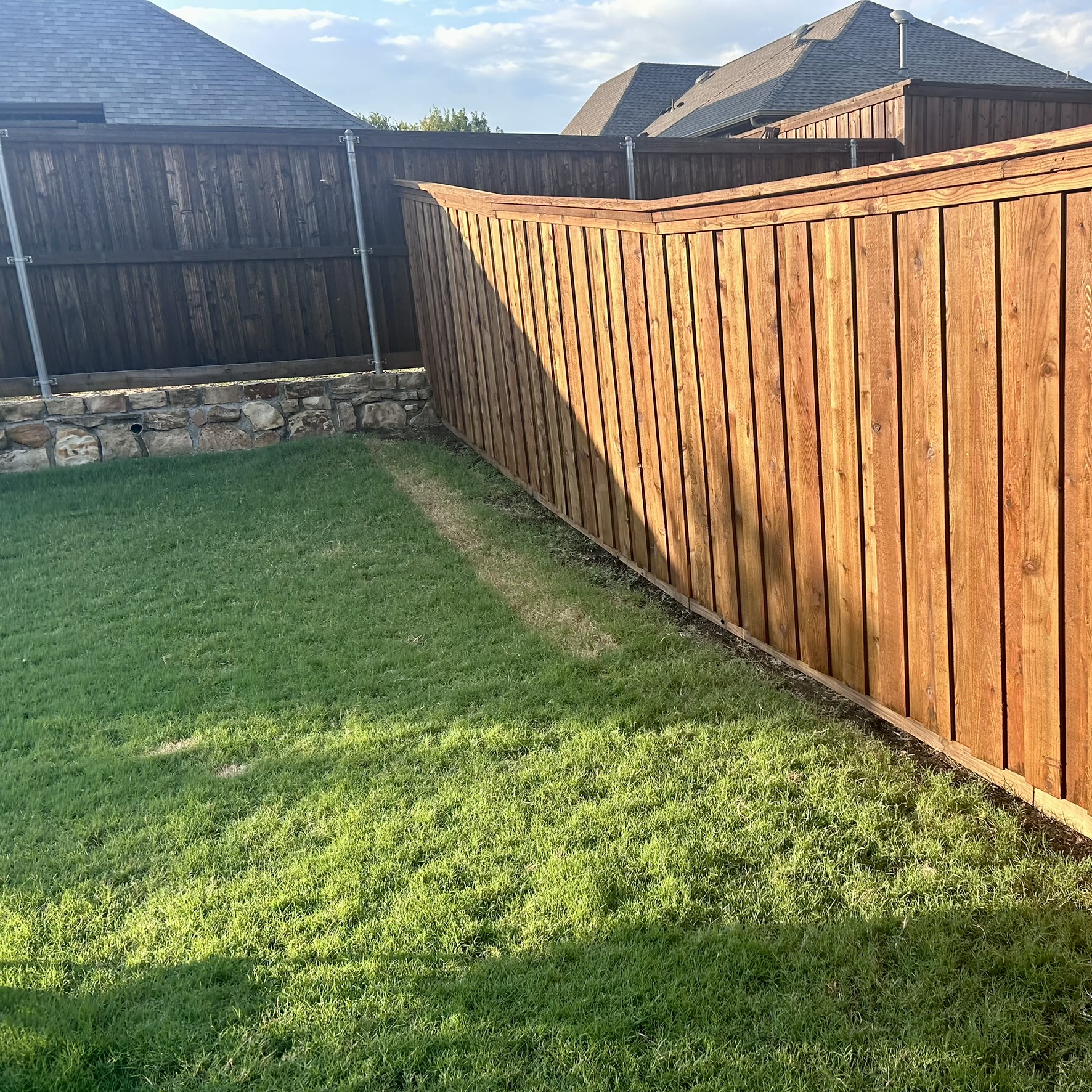 Cedar board-on-board privacy fence stepping down a slope with stone retaining wall