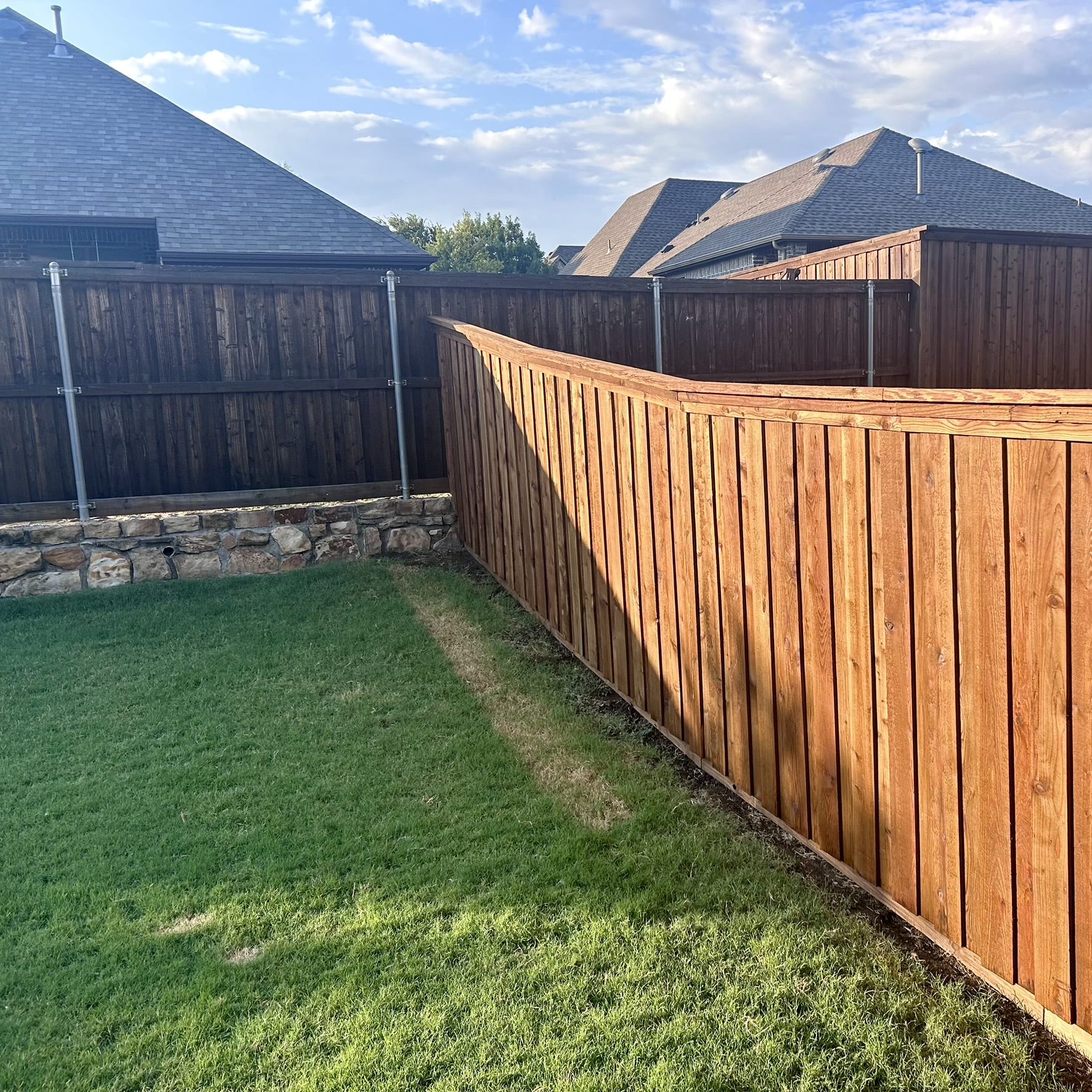 New cedar privacy fence with cap rail transitioning over a stone retaining wall