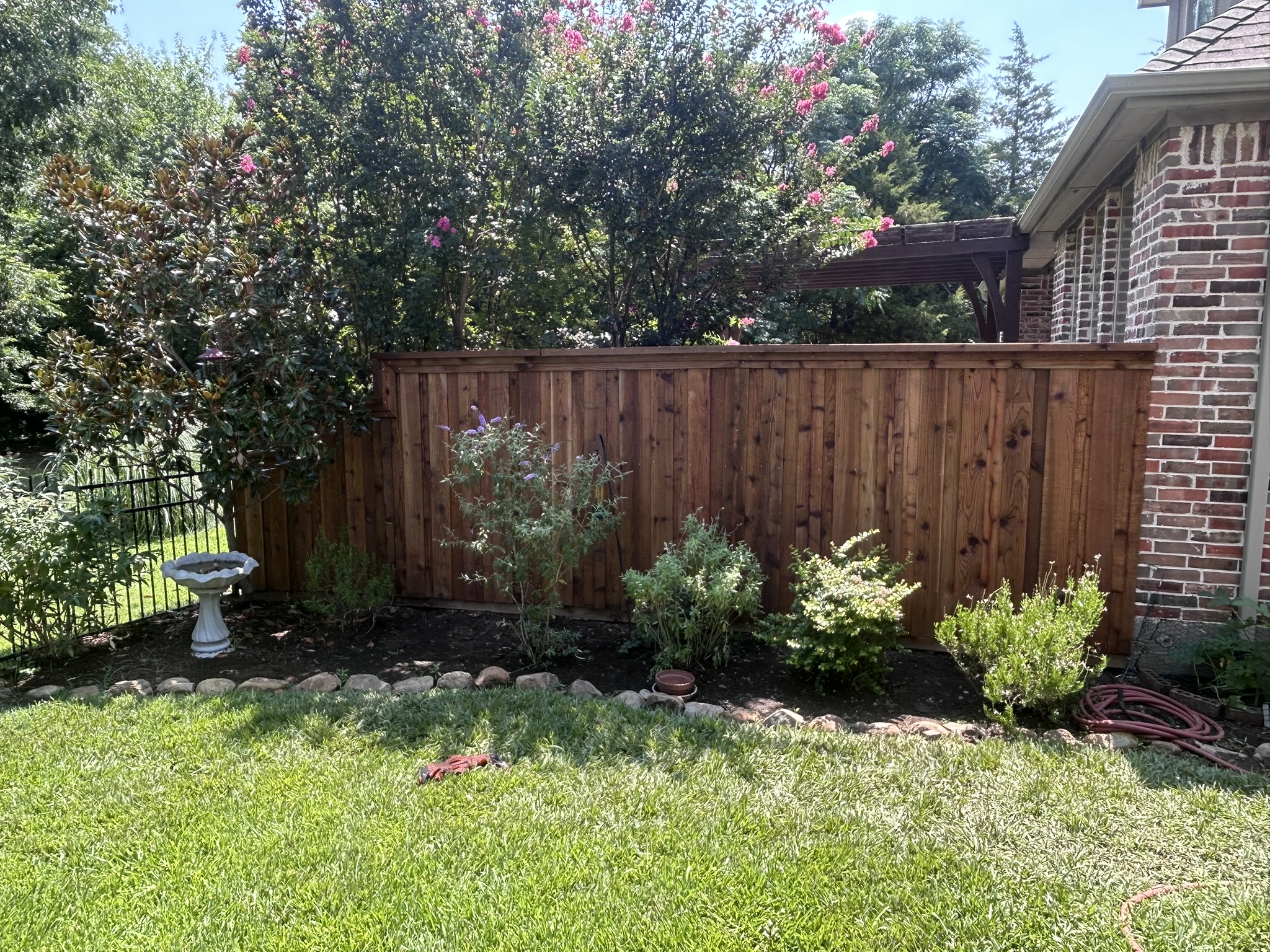 Stained cedar privacy fence with cap rail beside a brick home with landscaped garden