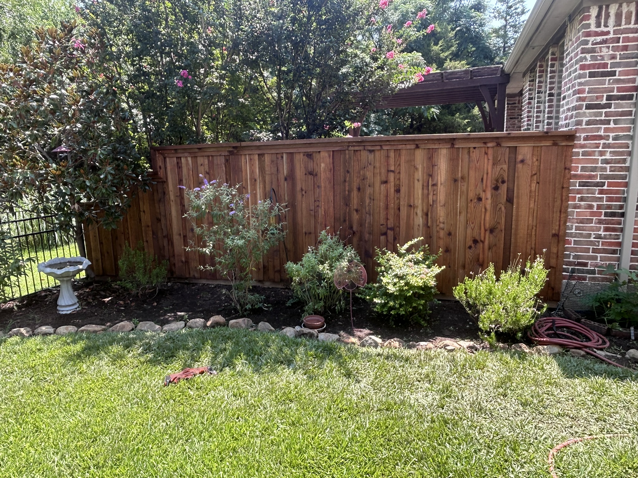 Stained cedar privacy fence in a front yard garden with bird bath and shrubs
