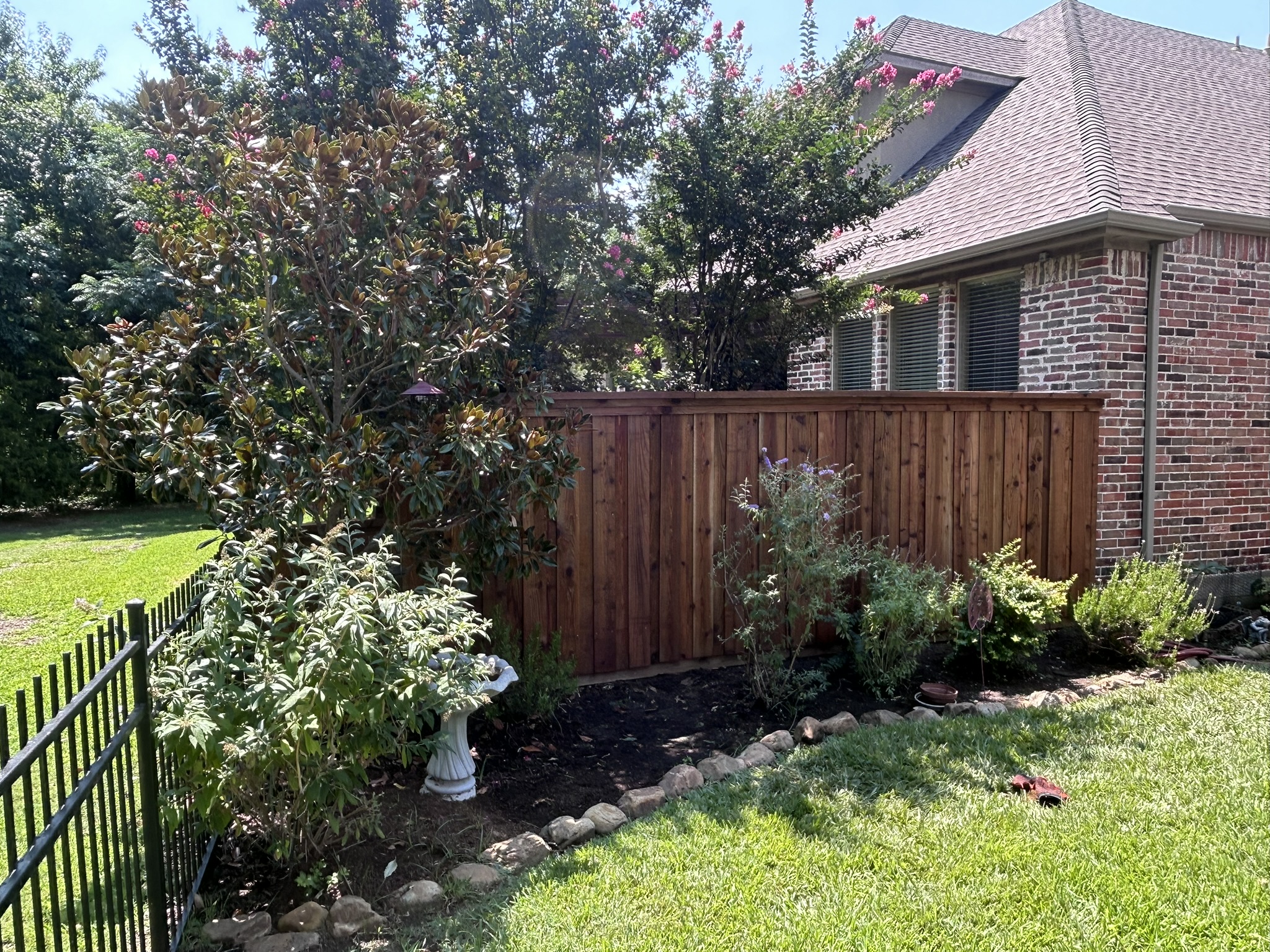 Stained cedar privacy fence with metal iron fence visible at corner near a brick house