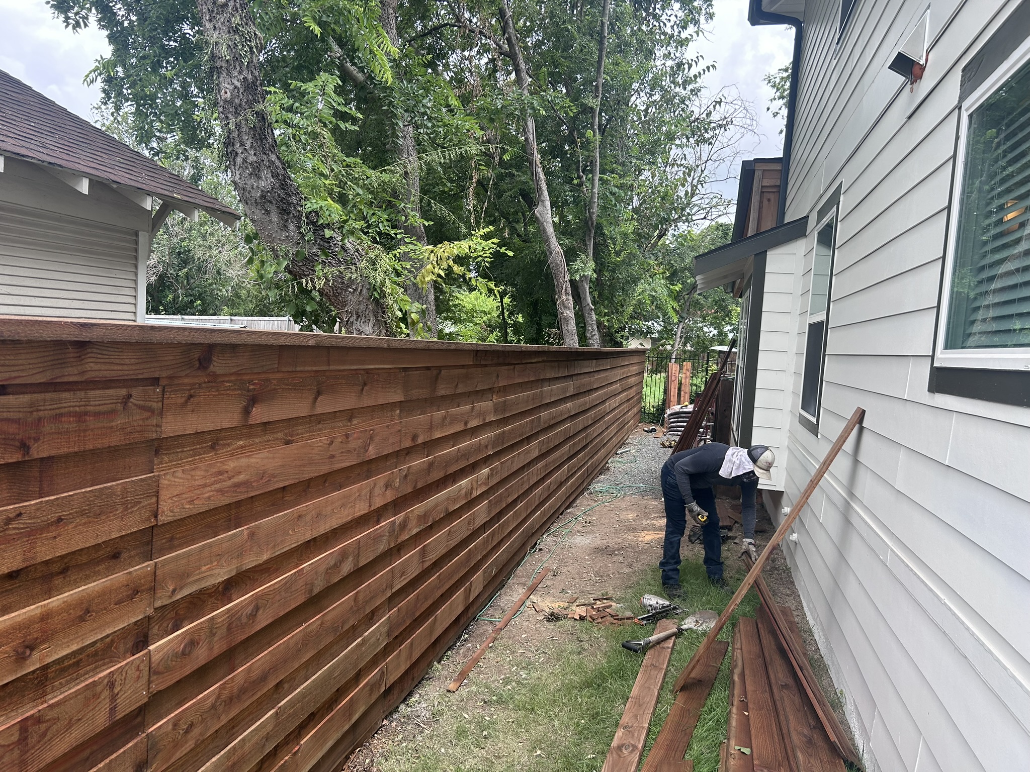 Horizontal slat cedar fence being installed along a narrow side yard